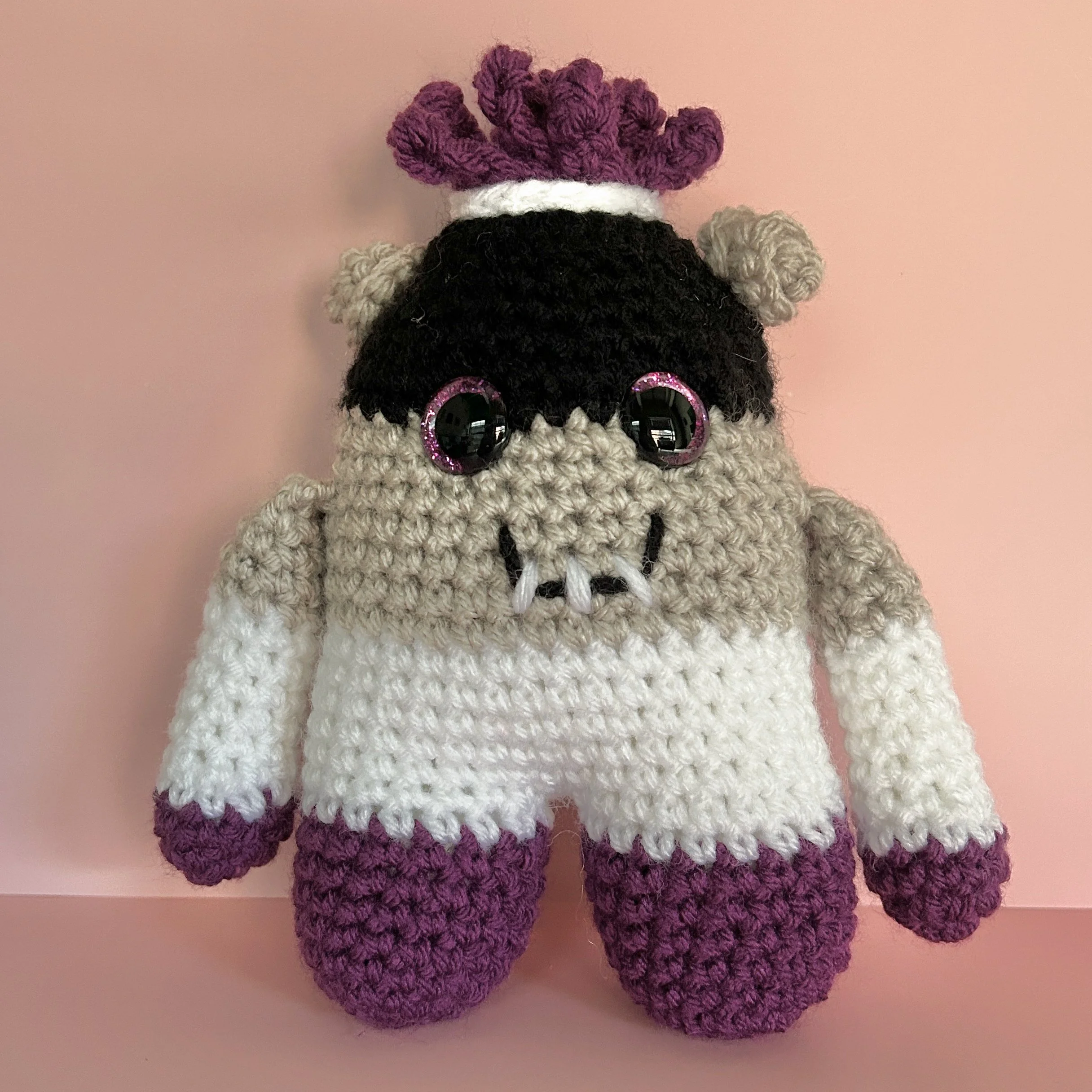 friendly black, grey, white, and purple striped monster with bun ears and short purple curly hair, purple googly eyes smiling with 3 teeth