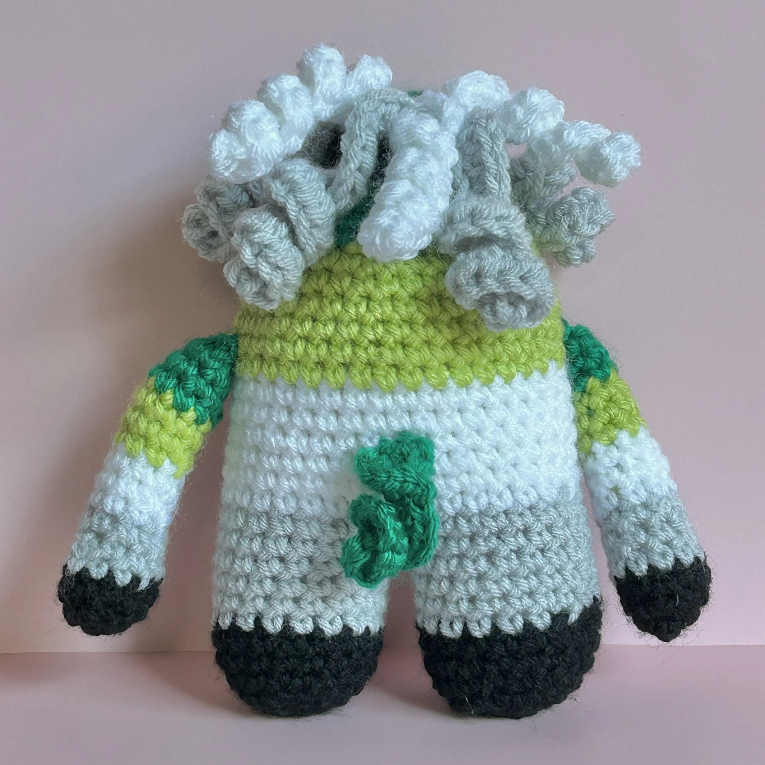 back of green, light green, white, gray, black striped monster with white, grey, green curly hair and curly green tail