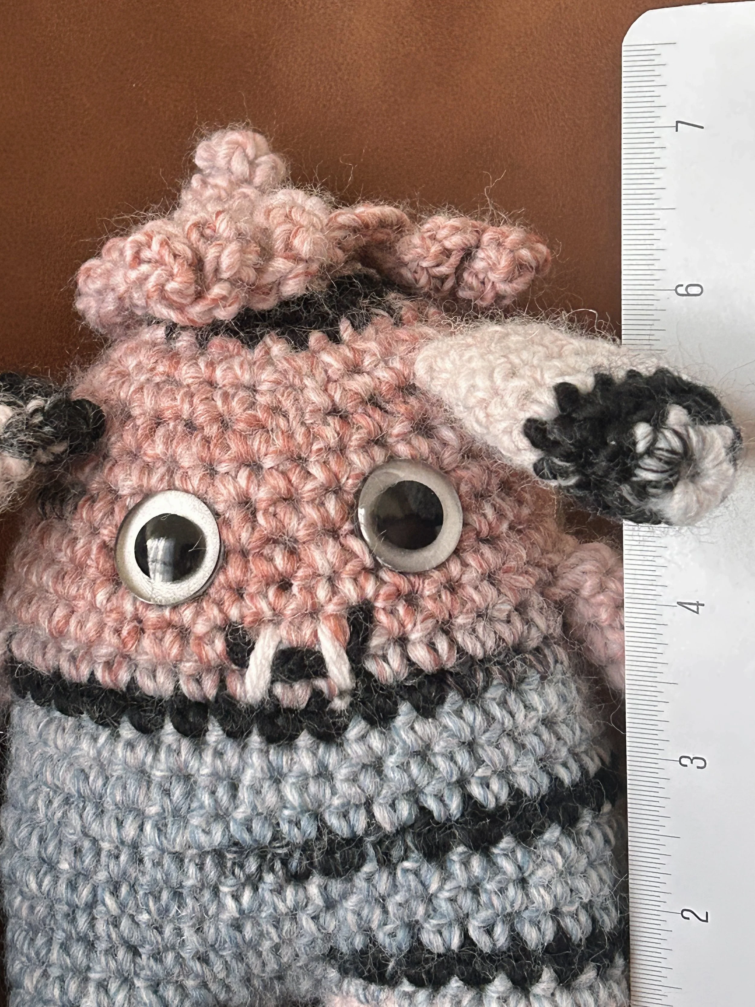 Dusty closeup of face light pink blue black monster long floppy ears curly hair googly eyes smiling with 2 teeth next to ruler about 6-1/4 inches tall