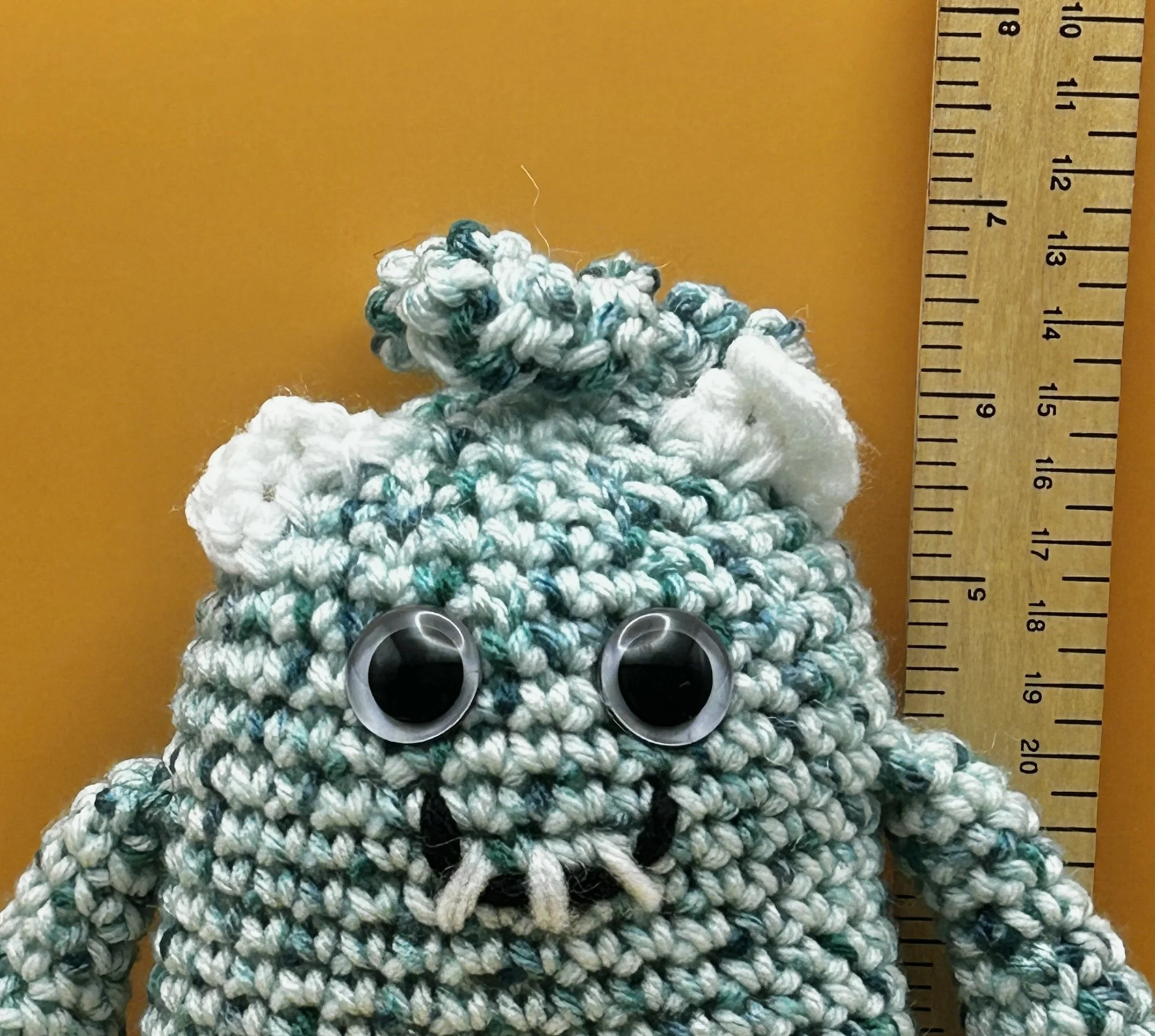 Sprout closeup of face green and white monster with squiggly hair white ears googly eyes smiling with 3 teeth next to ruler body about 6 inches tall