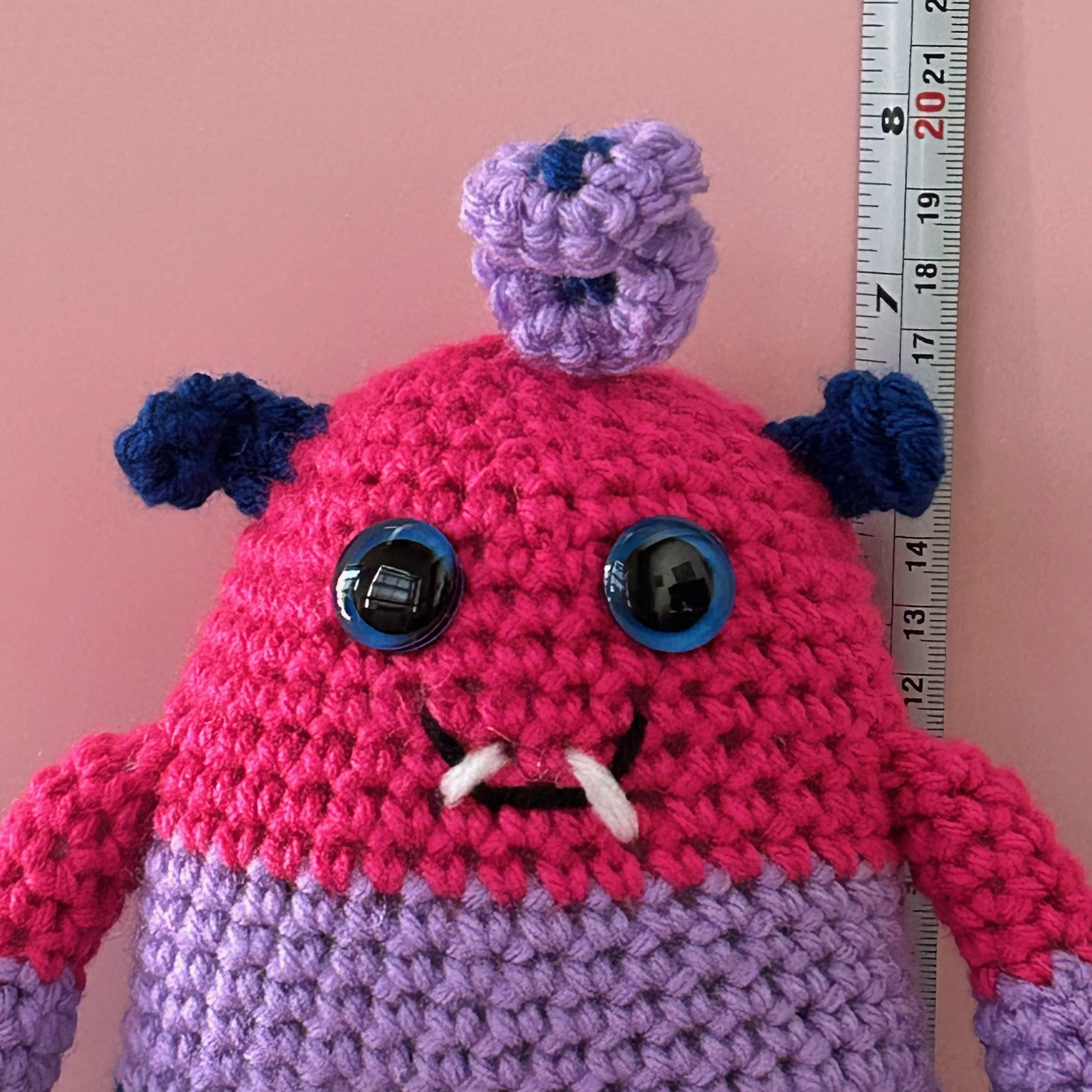 friendly monster plushie bisexual pride flag magenta lavender royal blue stripes blue googly eyes blue ears purple squiggle hair smiling with 2 teeth in front of ruler body about 6-1/2 inches tall