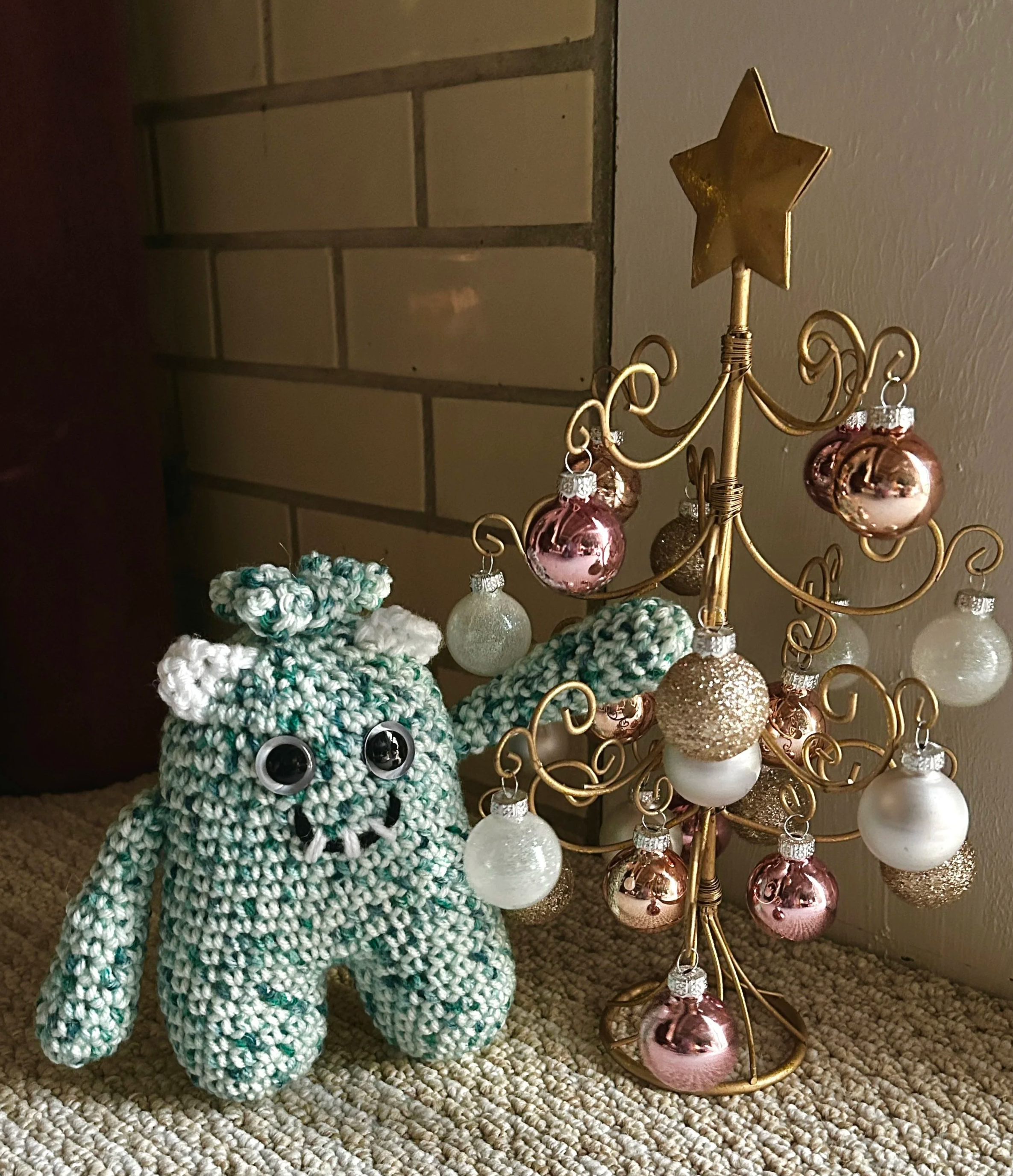 Sprout green and white monster with squiggly hair white ears googly eyes smiling with 3 teeth with gold Christmas tree with rose gold and white round ornaments