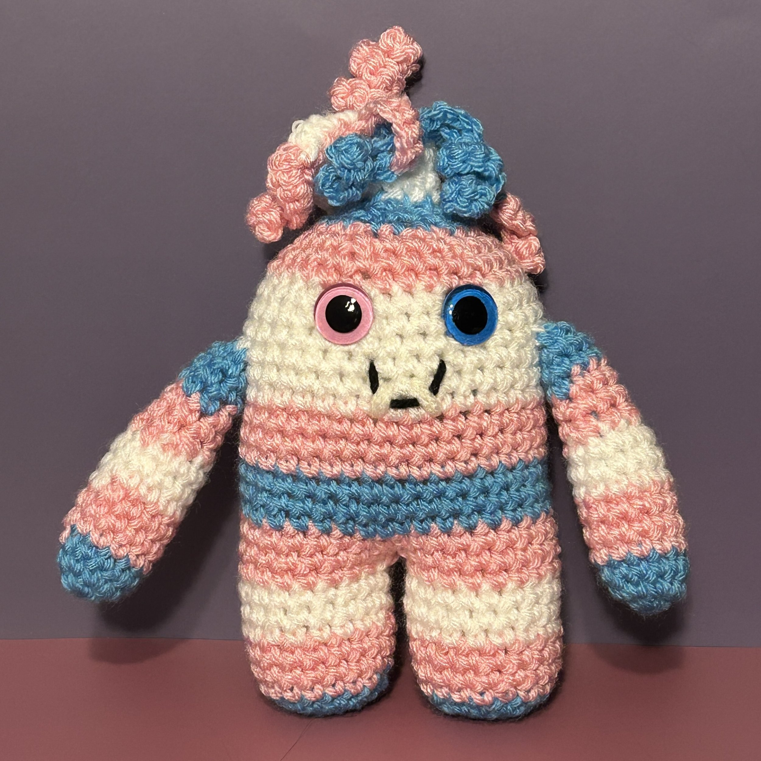 Mel light blue pink and white striped monster with mass of pink, blue, and white curly hair, one pink and one blue googly eye, smiling with 2 teeth (Copy)