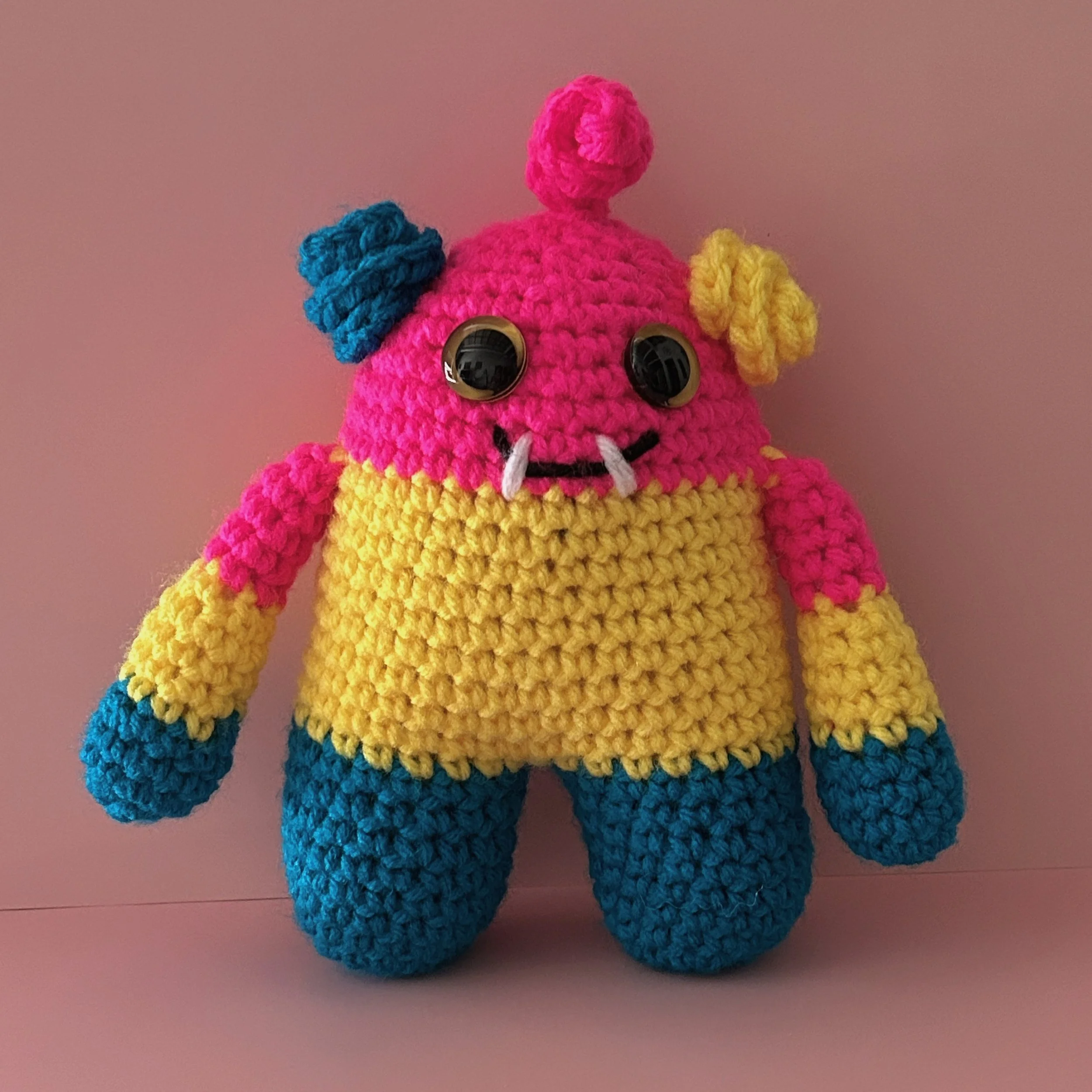 friendly bright pink yellow and blue striped monster with curly ears and a pink squiggle hair yellow googly eyes smiling with two teeth