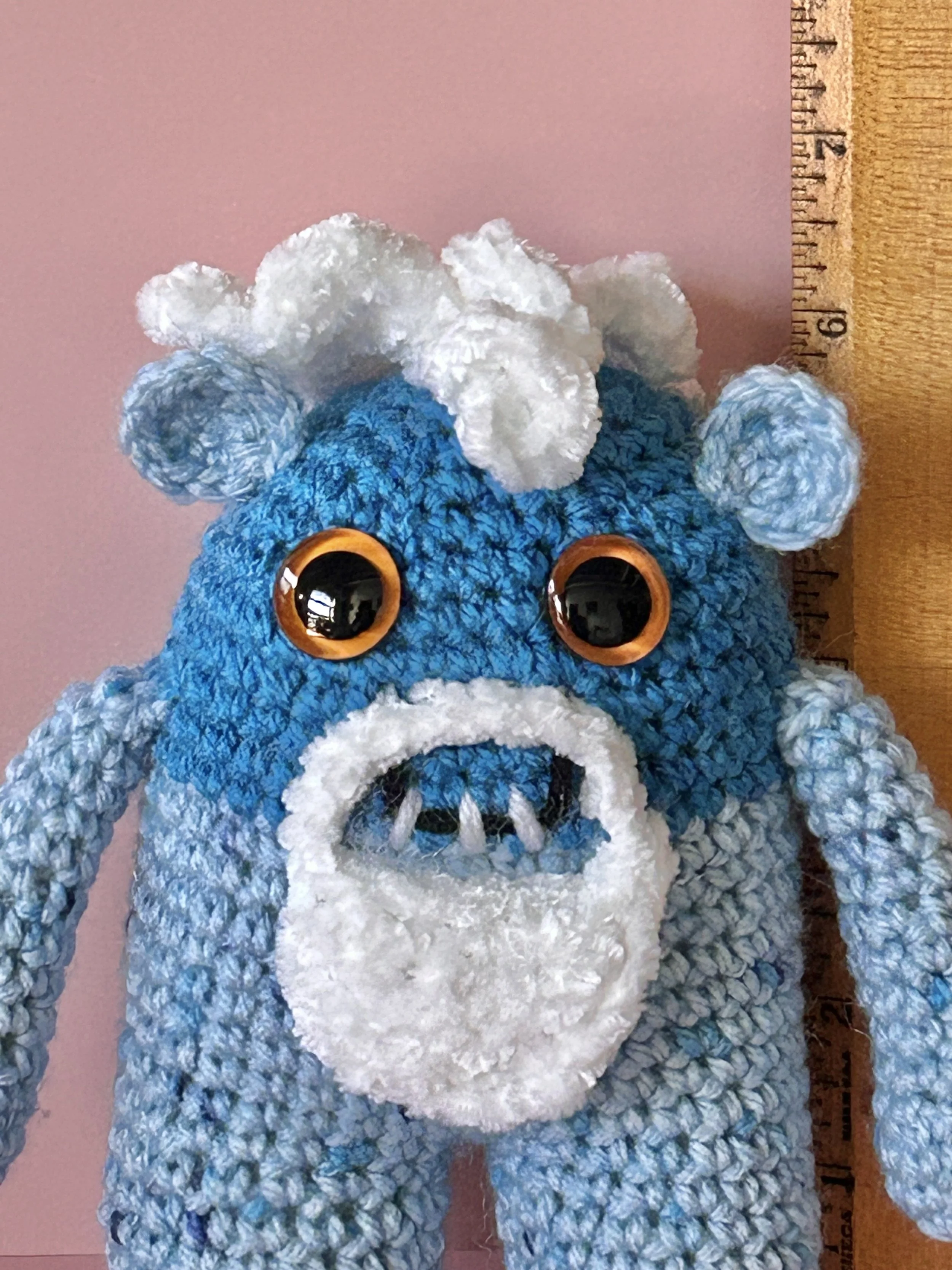 Snowbeard closeup of face light blue monster with white fluffy beard white squiggle hair orange googly eyes round blue ears eyes smiling with 3 teeth next to ruler body about 6 inches tall