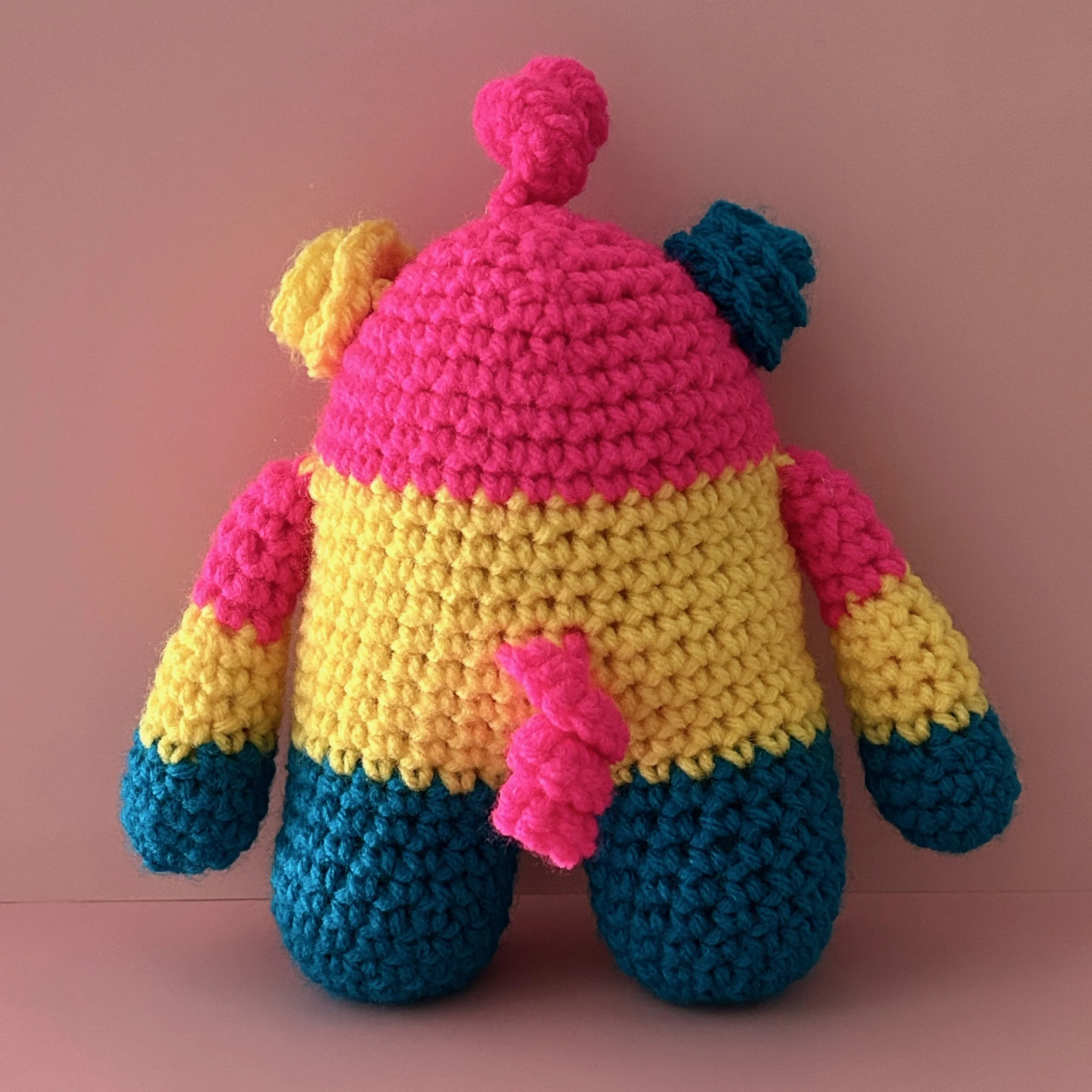 back of bright pink yellow and blue striped monster with curly ears and a pink squiggle hair and tail
