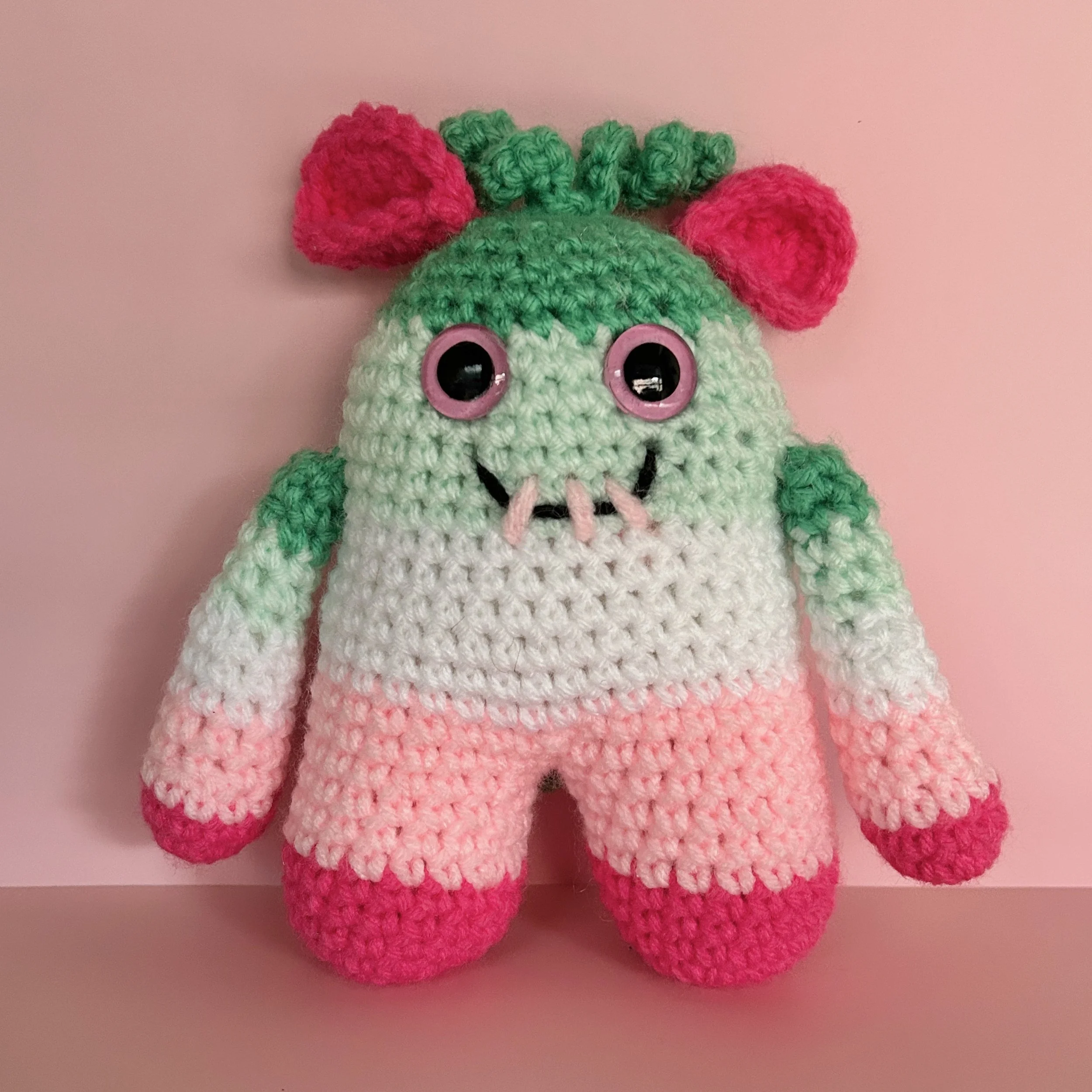 friendly green, white, and pink striped monster with bright pink folded ears squiggly jade green hair pink googly eyes smiling with 3 teeth