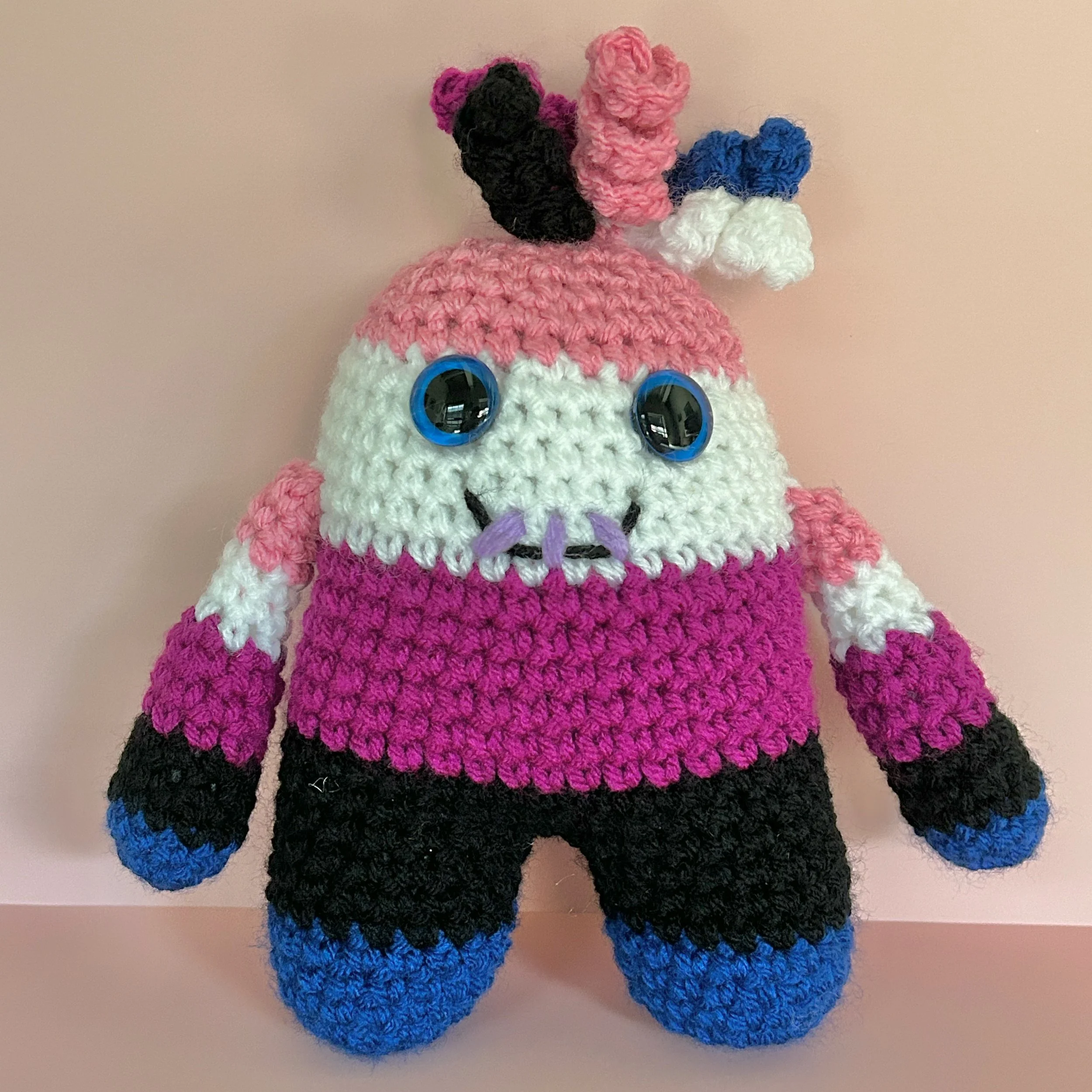 friendly pink, white, purple, black, and blue striped monster with squiggly hair blue googly eyes smiling with 3 teeth