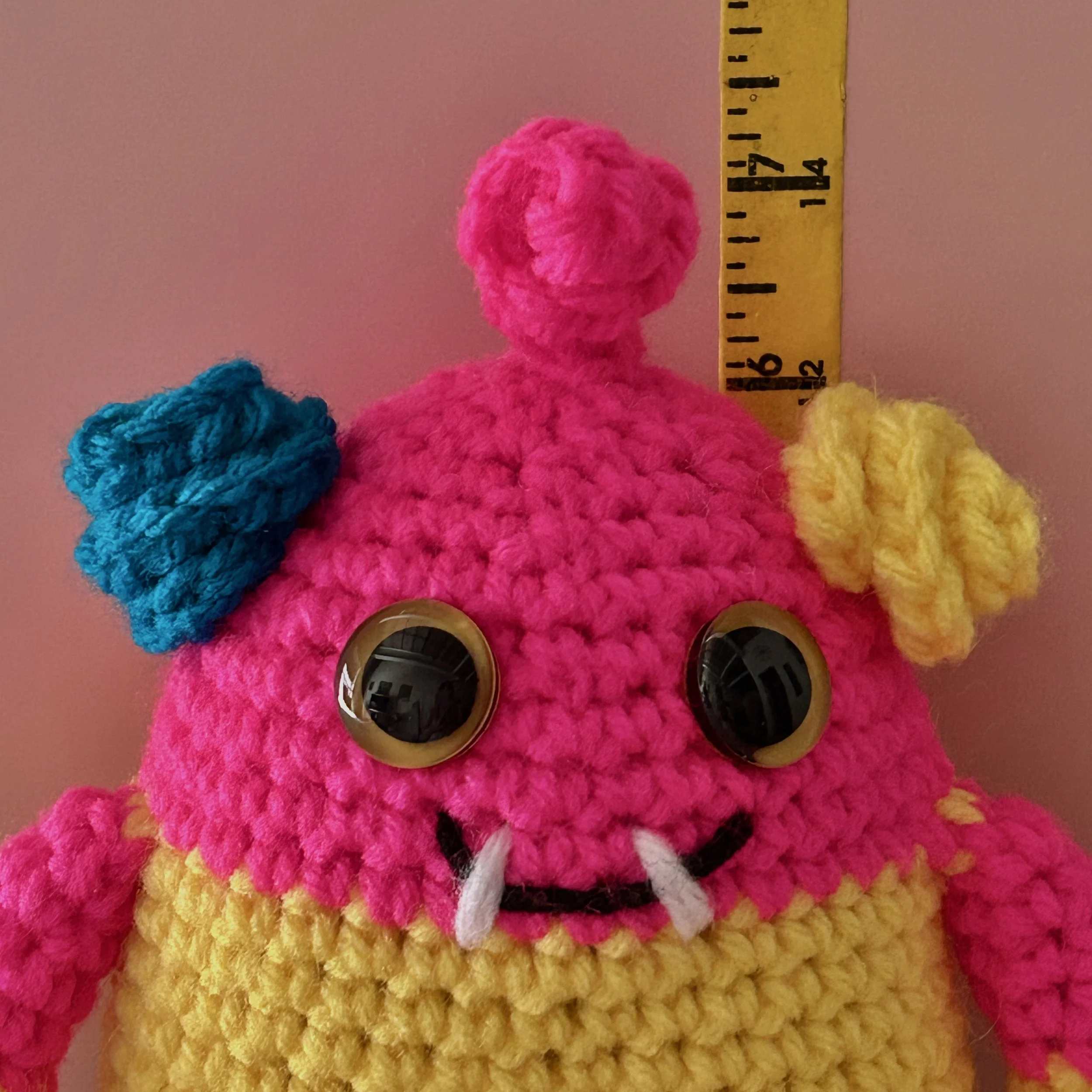 closeup of friendly bright pink yellow and blue striped monster with curly ears and a pink squiggle hair yellow googly eyes smiling with two teeth standing in front of ruler body about 6 inches tall