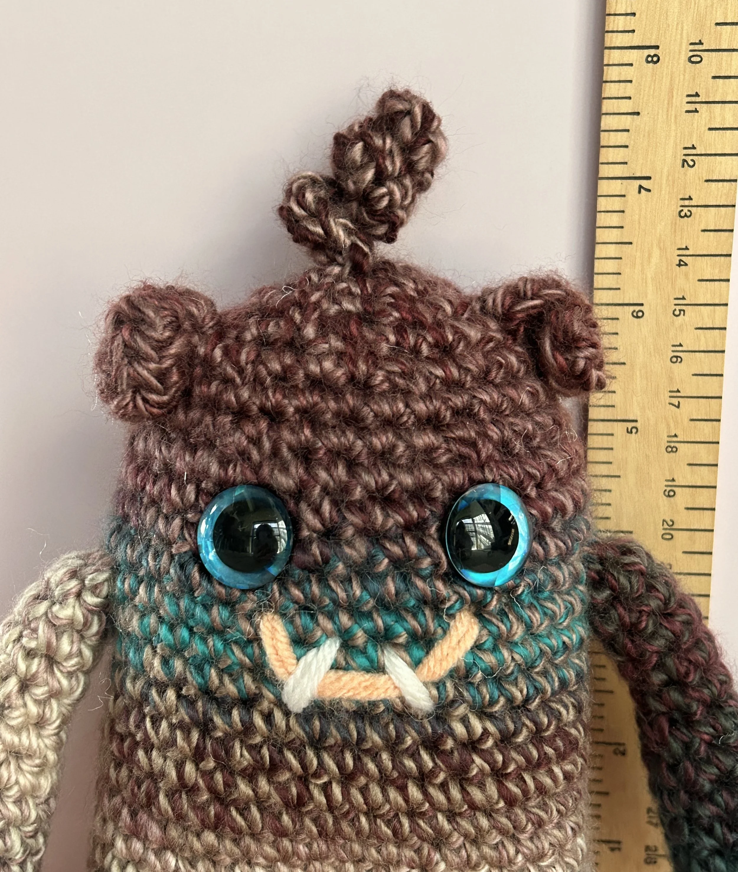 Plumly closeup of face plum teal taupe monster blue googly eyes squiggly hair smiling with 2 teeth next to ruler, body about 6-1/2 inches tall