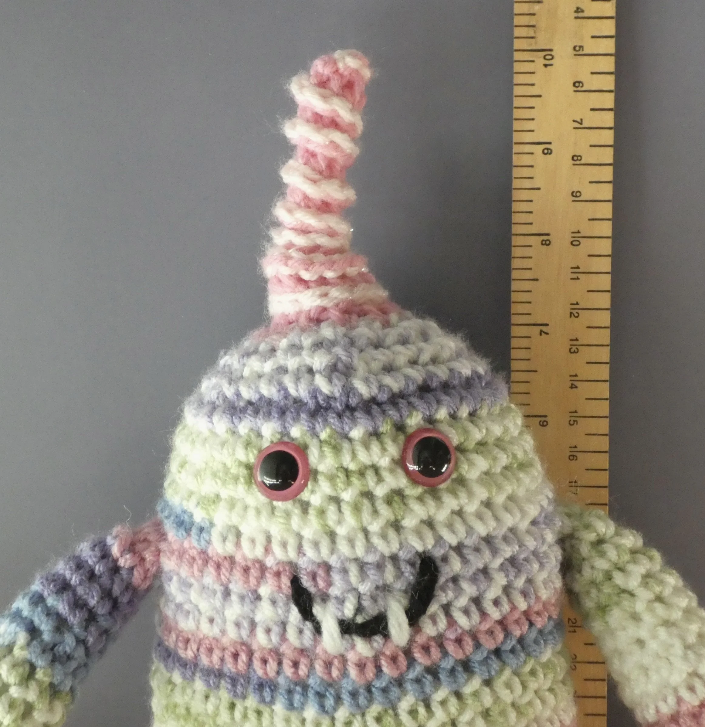 Quark closeup of face light purple pink and sparkly white striped monster with pink and white spiral horn pink beady eyes smiling with 2 teeth next to ruler body about 7-1/4  iches tall