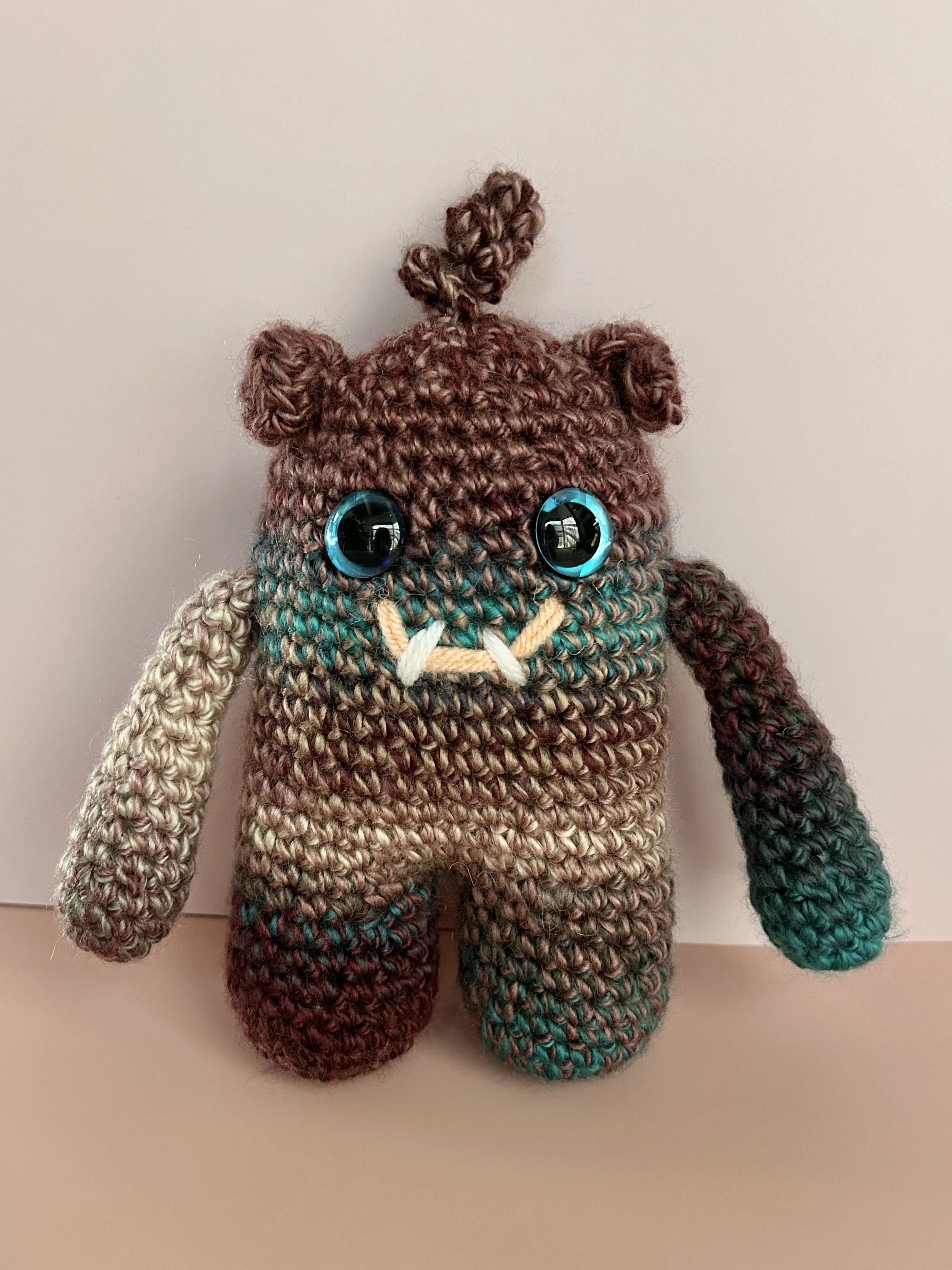 Plumly plum teal taupe monster with blue googly eyes squiggle hair smiling with 2 teeth