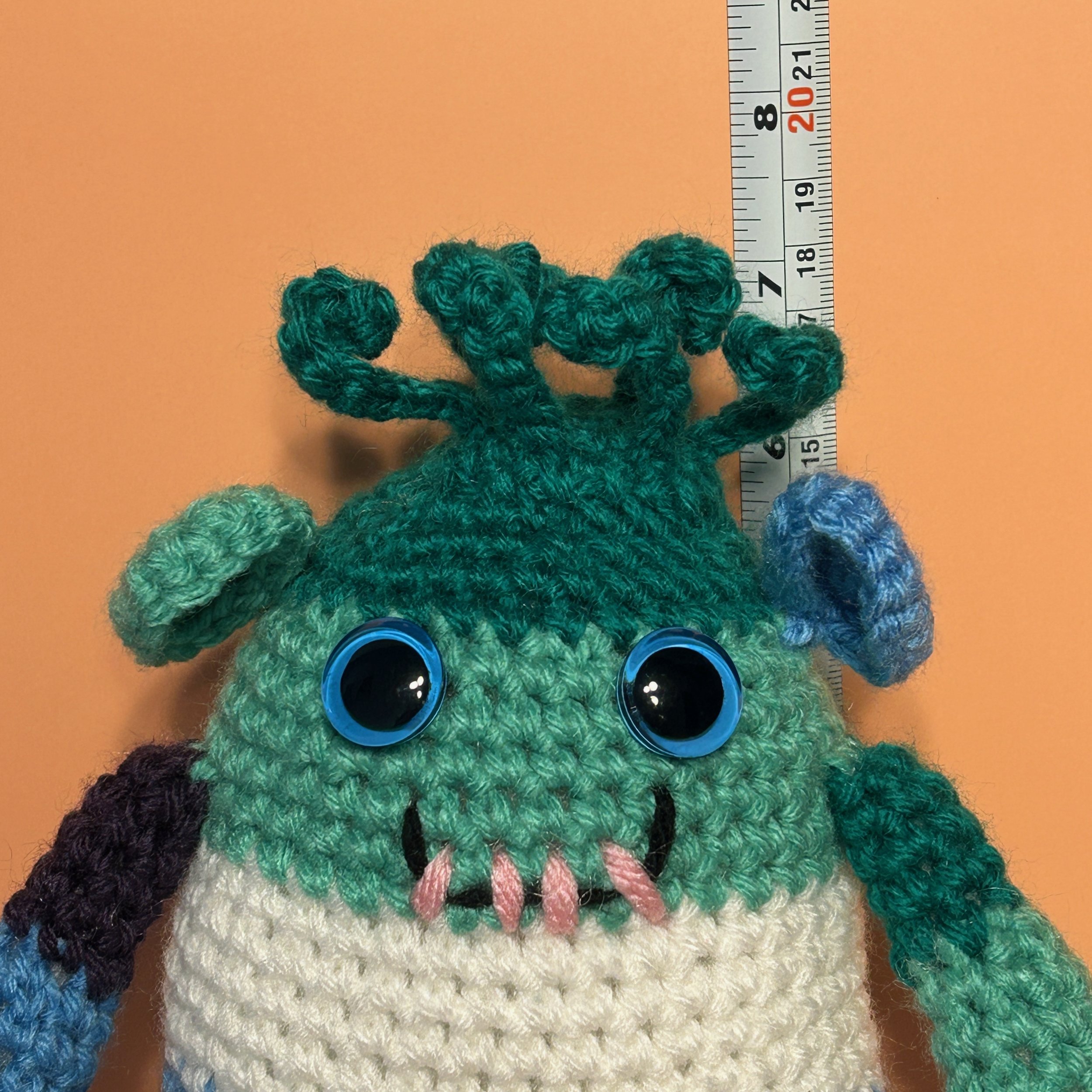 Jack green jade white light blue indigo striped monster with medusa-style hair, round ears, light blue googly eyes, smiling with four teeth in front of ruler, body about 6-1/4 inches tall