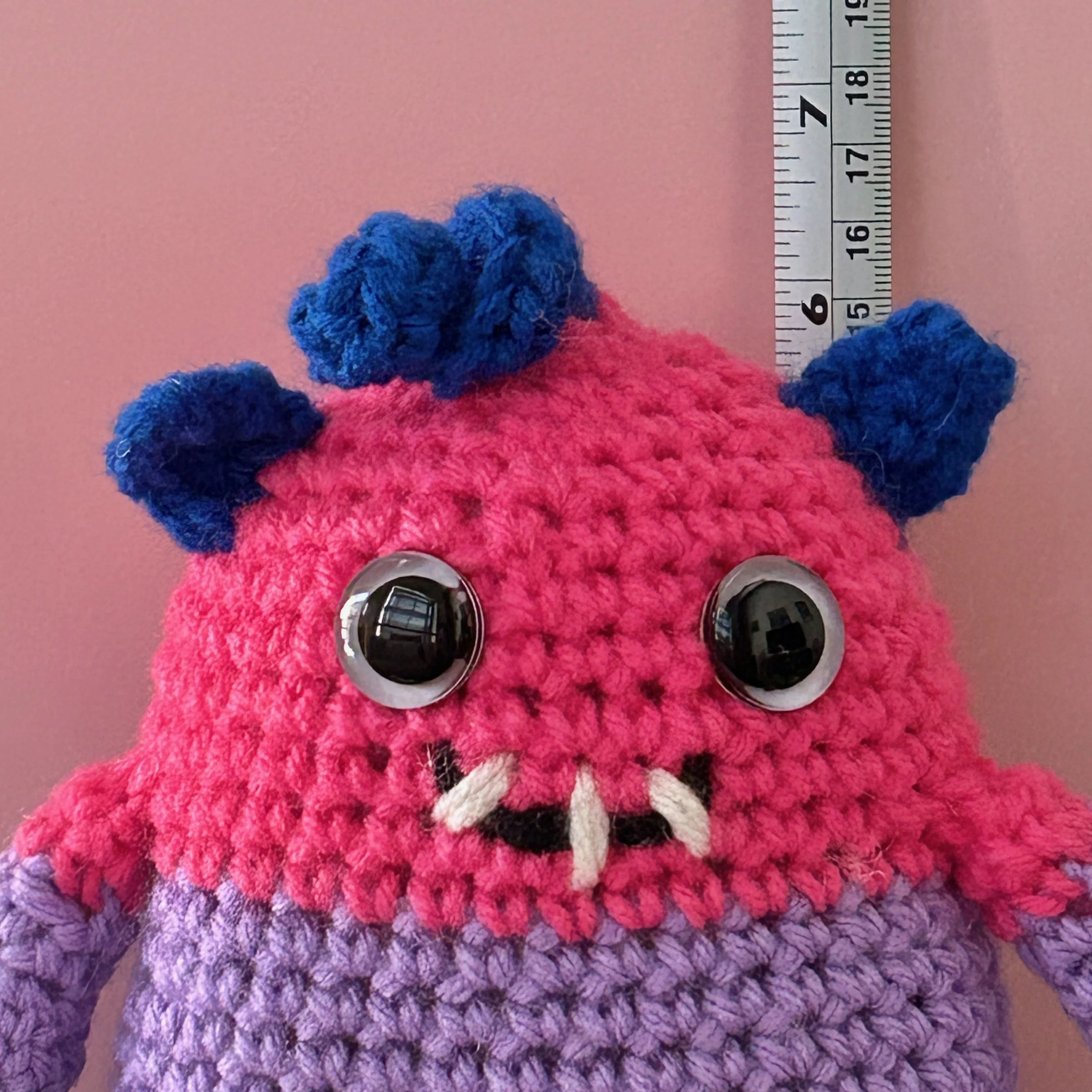 friendly monster plushie bisexual pride flag magenta lavender royal blue stripes googly eyes blue ears blue squiggle hair smiling with 3 teeth in front of ruler body about 6 inches tall