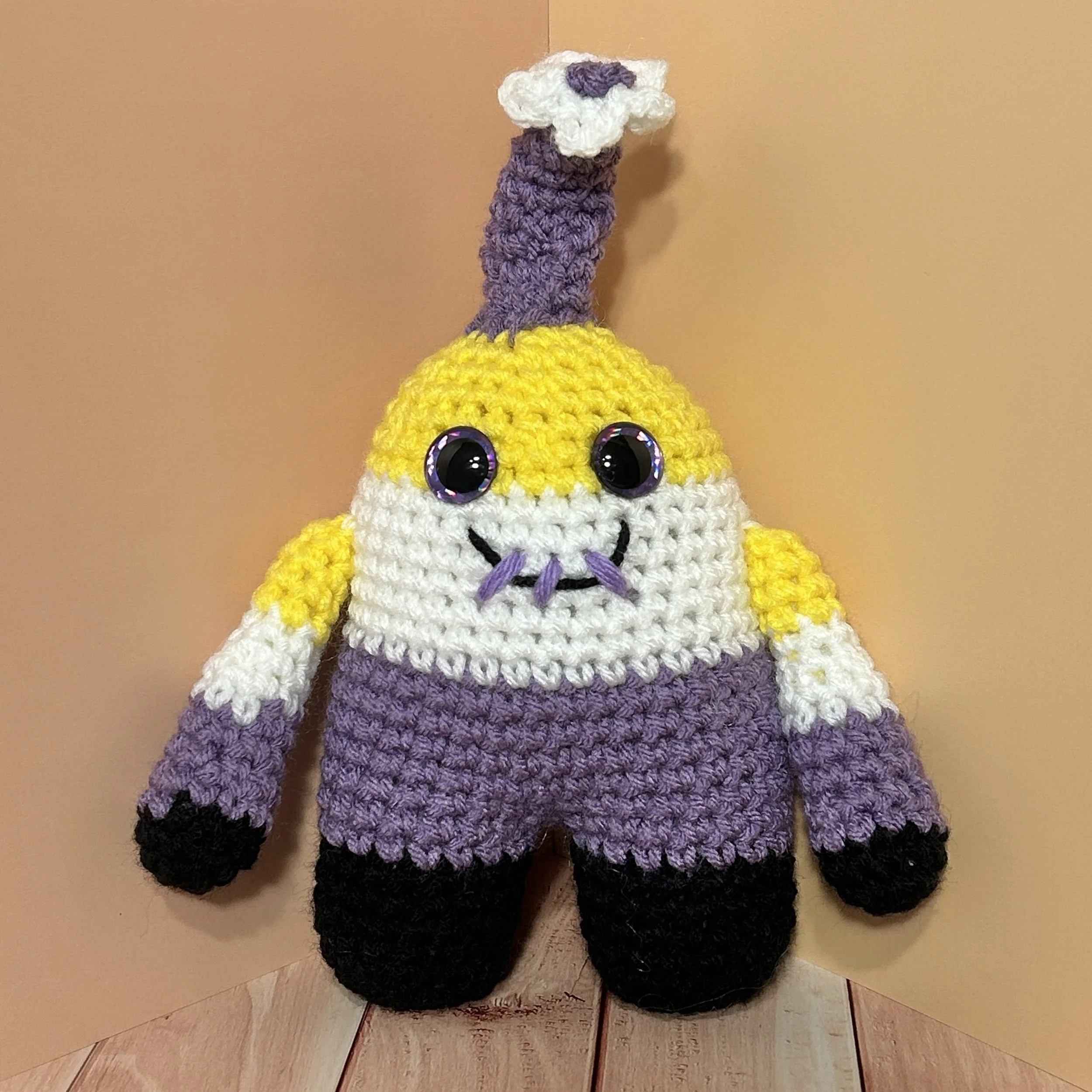 Kye yellow white purple black striped monster with purple horn topped with white flower, purple googly eyes, smiling with 3 teeth