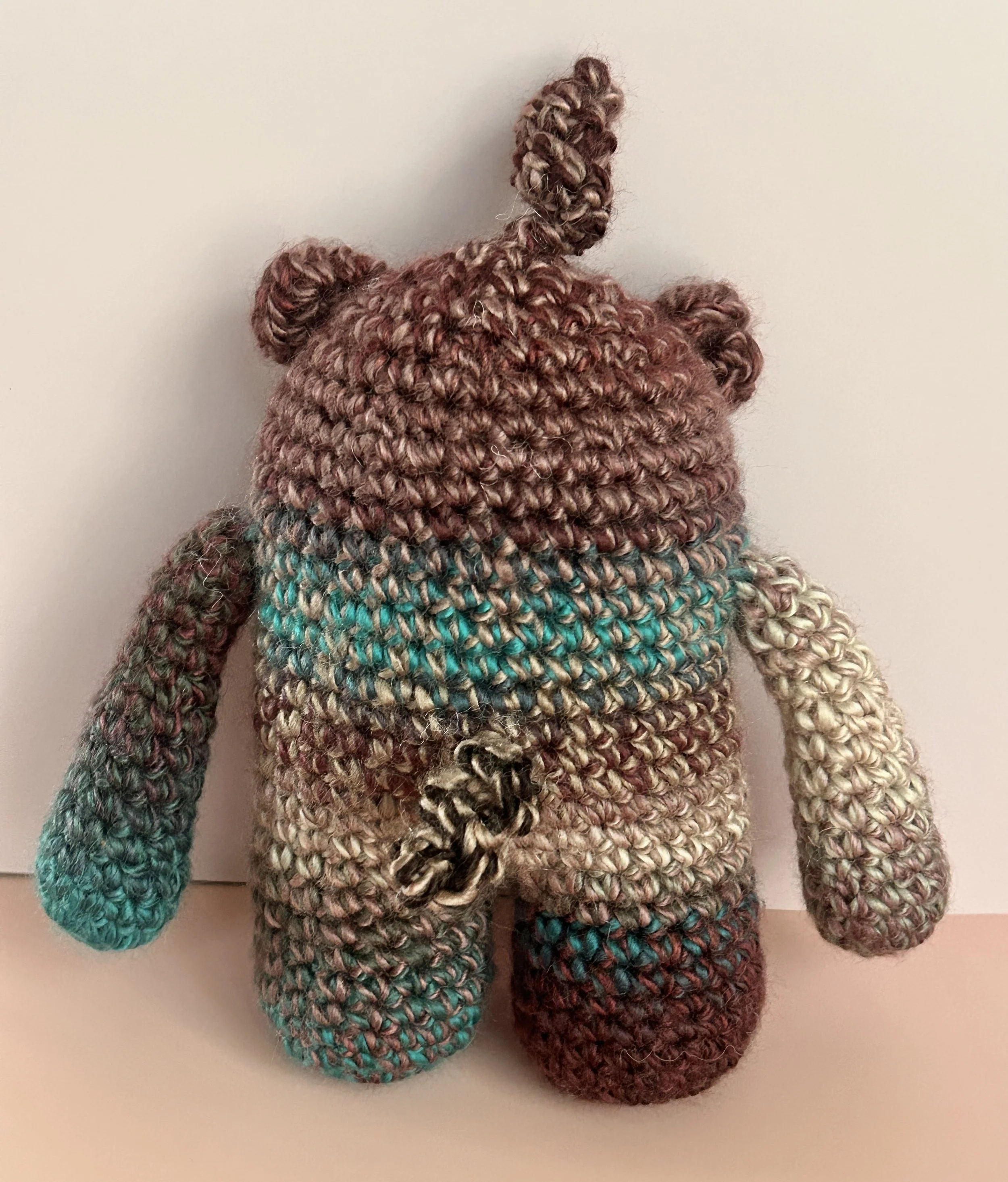 Plumly back of plum teal taupe monster with squiggly hair and curly tail