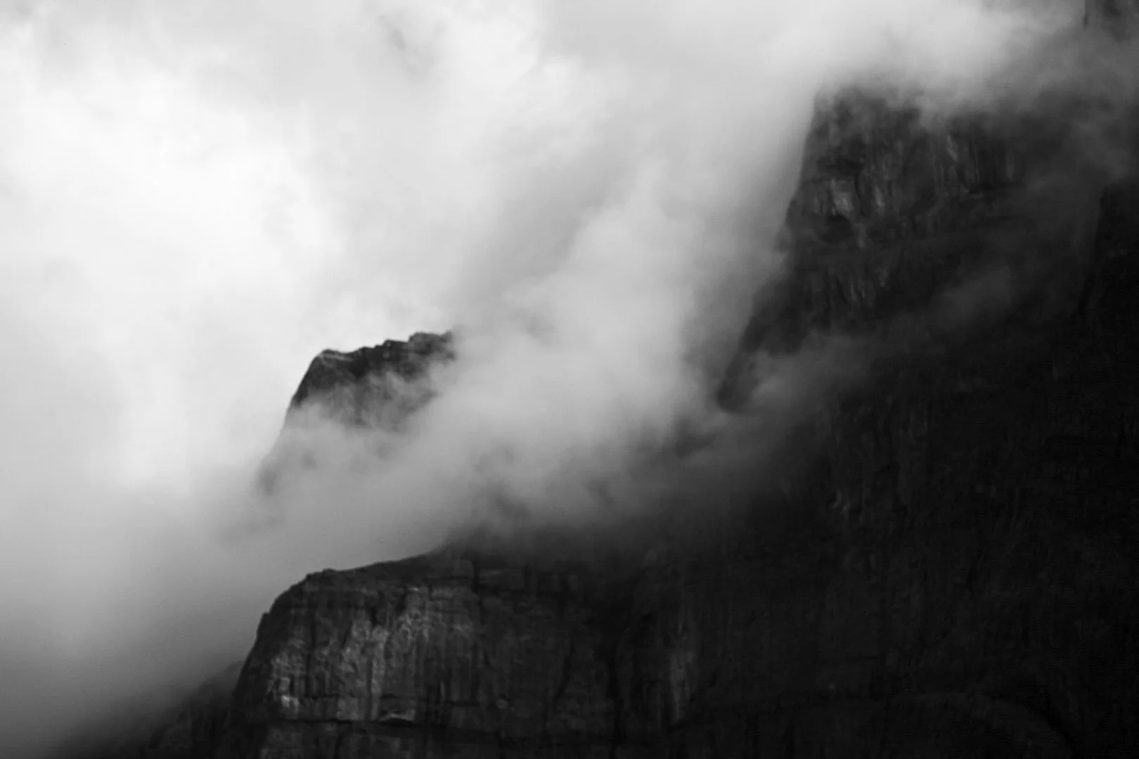 Black and white photograph of mountain peaks shrouded in thick clouds and mist.