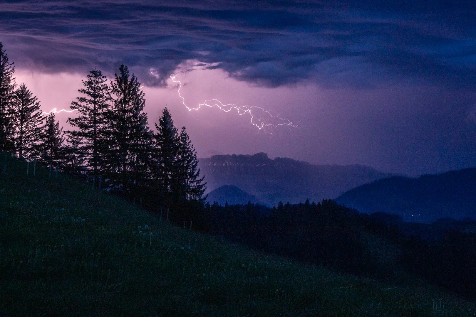 Lightning storm over a forested mountain landscape in the Emmental valley at night.