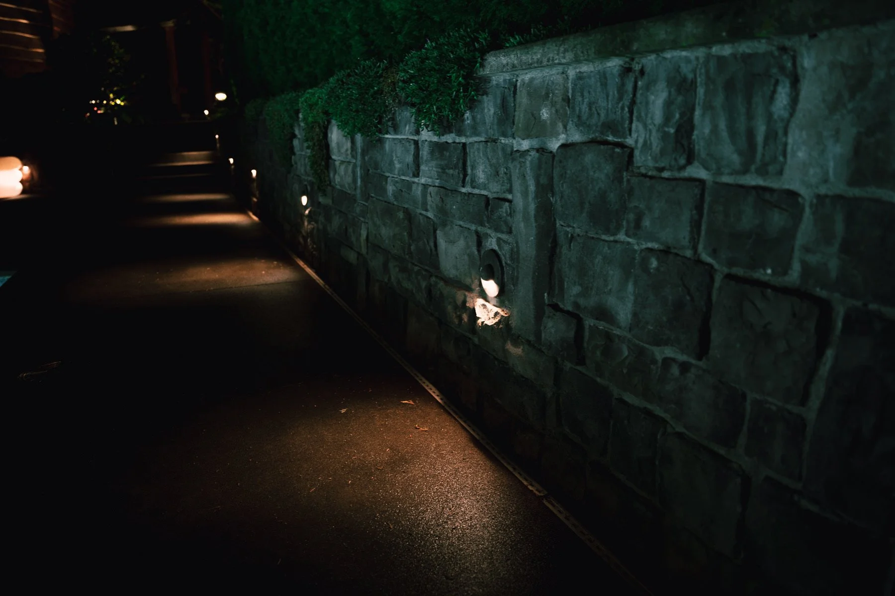 A stone wall with outdoor lighting along a pathway at night.