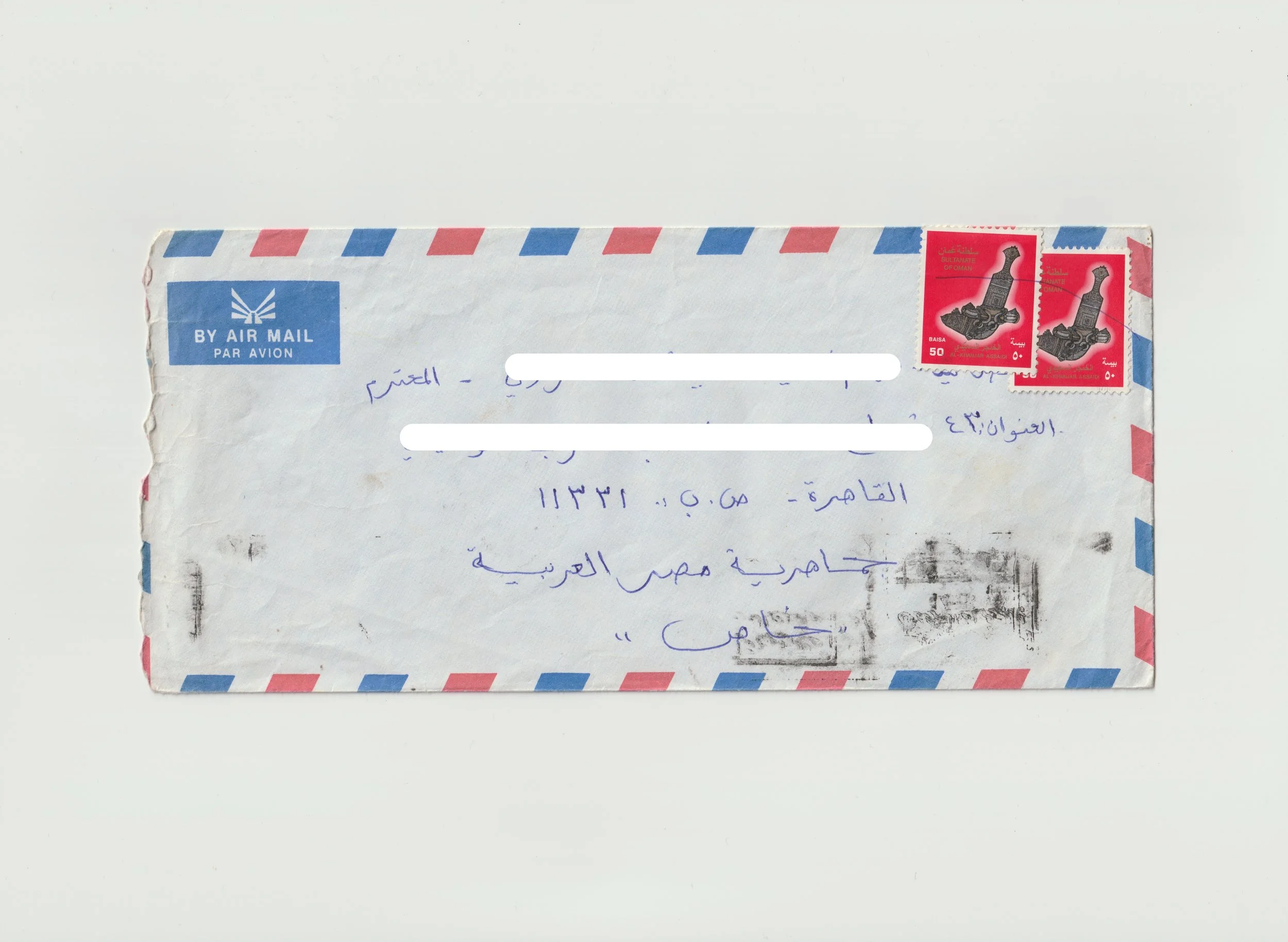 A white airmail envelope with red and blue border stripes, two red stamps featuring black cannon illustrations, handwritten Arabic address, and a blue