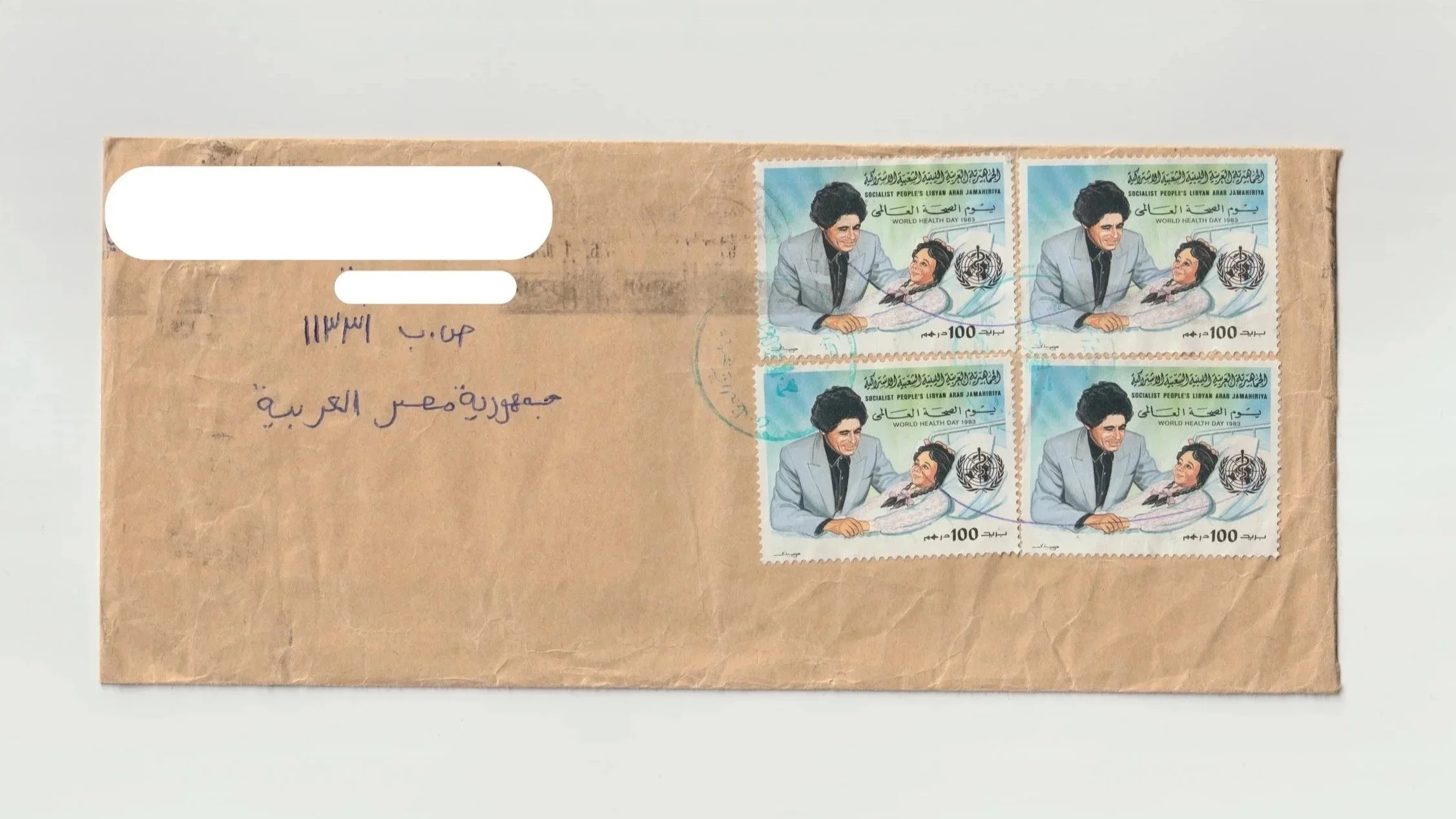 A brown envelope with four identical postage stamps depicting a woman in a gray suit with a black hairdo, smiling, holding a child's hand, with the World Health Organization logo and Arabic text.