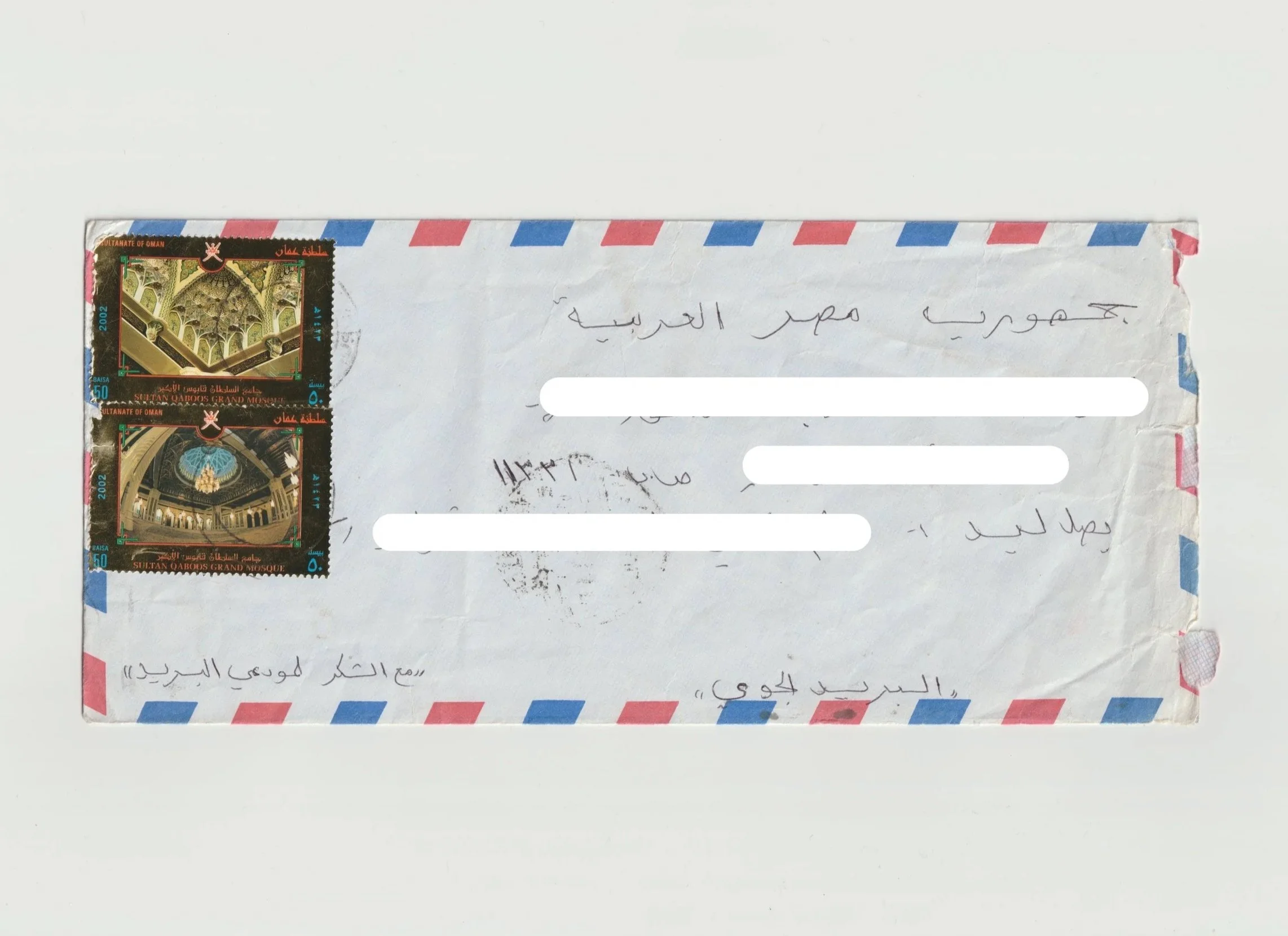 Envelope with red, white, and blue border, two postage stamps showing the interior of a mosque, handwritten Arabic address, and a postal cancellation mark.