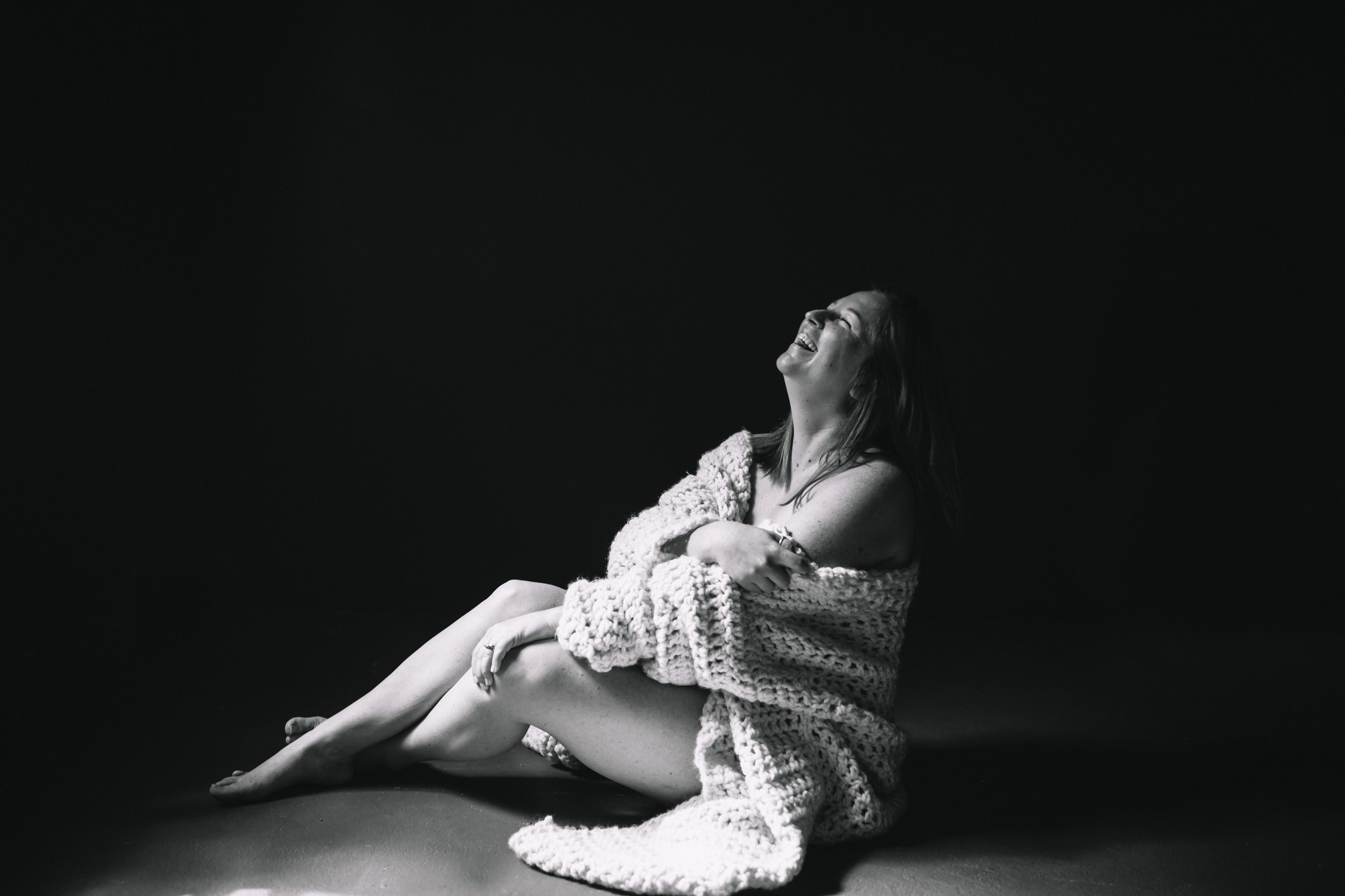Woman laughing wrapped in a chunky knit blanket in a dark studio, authentic raw portrait by Emily Scott, Beaufort SC