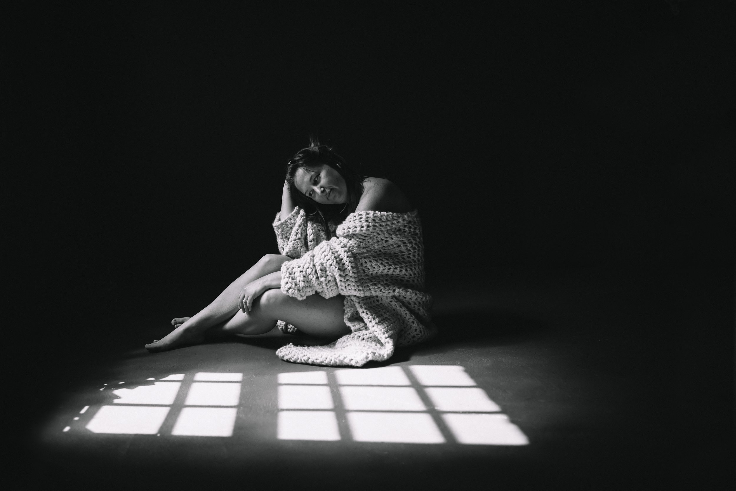 Woman wrapped in a knit blanket with dramatic window grid light shadows on the floor, fine art nude photography, Boudoir by Emily, South Carolina