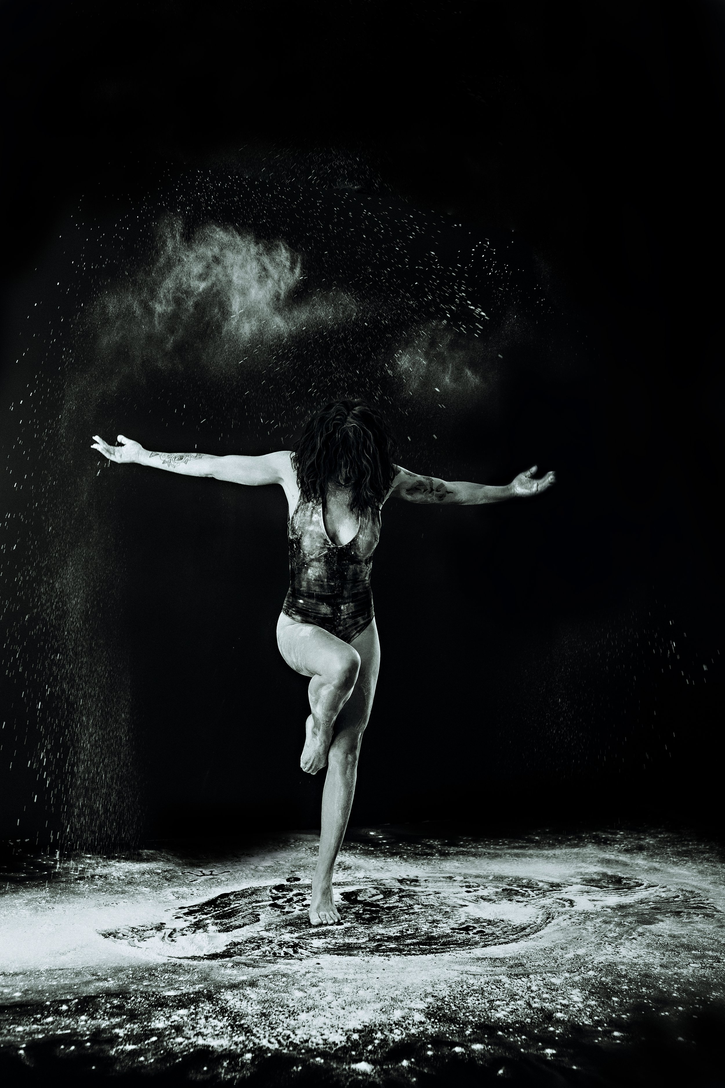 Dramatic black and white fine art portrait of a woman dancing with arms outstretched in a powder explosion, artistic photography by Emily Scott, South Carolina