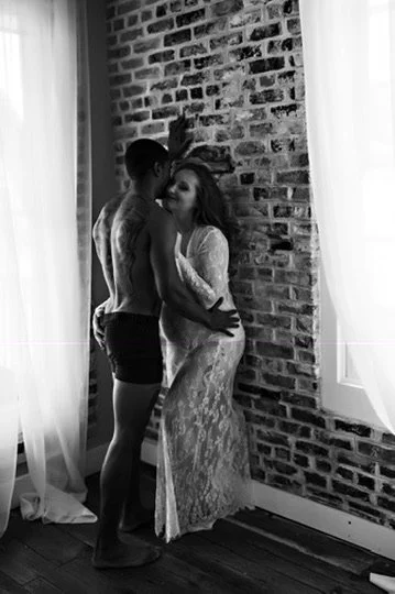 Black and white couples boudoir portrait of two partners embracing against an exposed brick wall, Boudoir by Emily, Beaufort SC