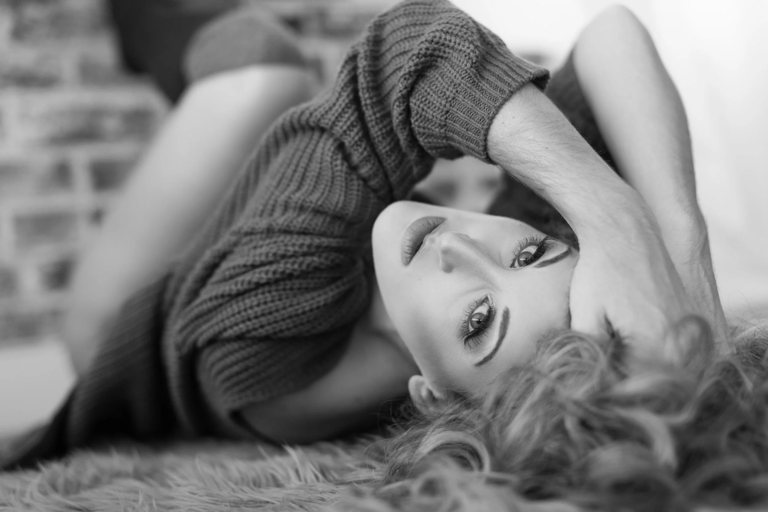 Black and white boudoir portrait of a woman in a sweater laying on the floor looking back at the camera, fine art photography by Emily Scott, South Carolina