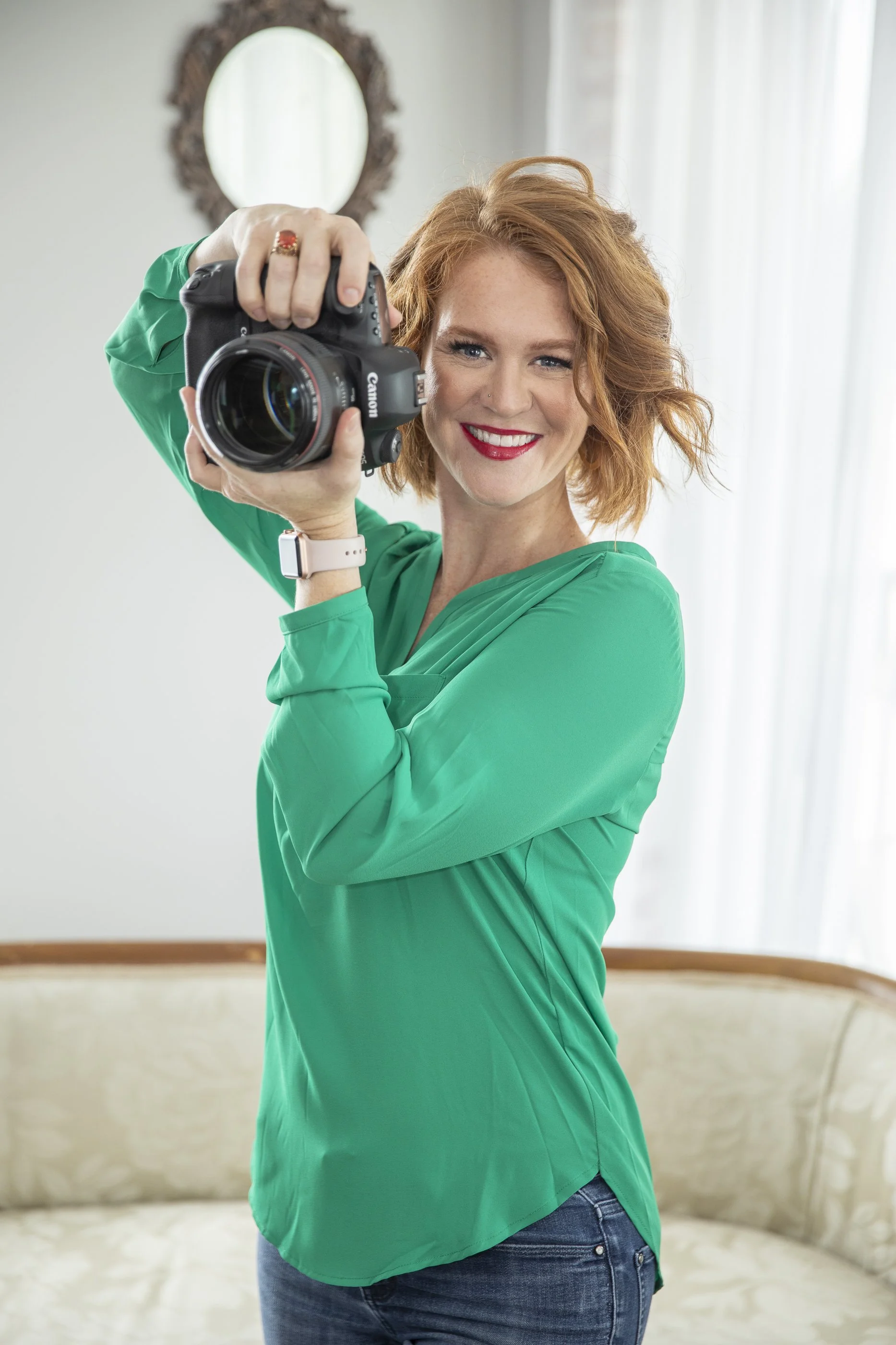 Emily Scott, boudoir photographer in Beaufort SC, smiling and holding her Canon camera in her natural light studio