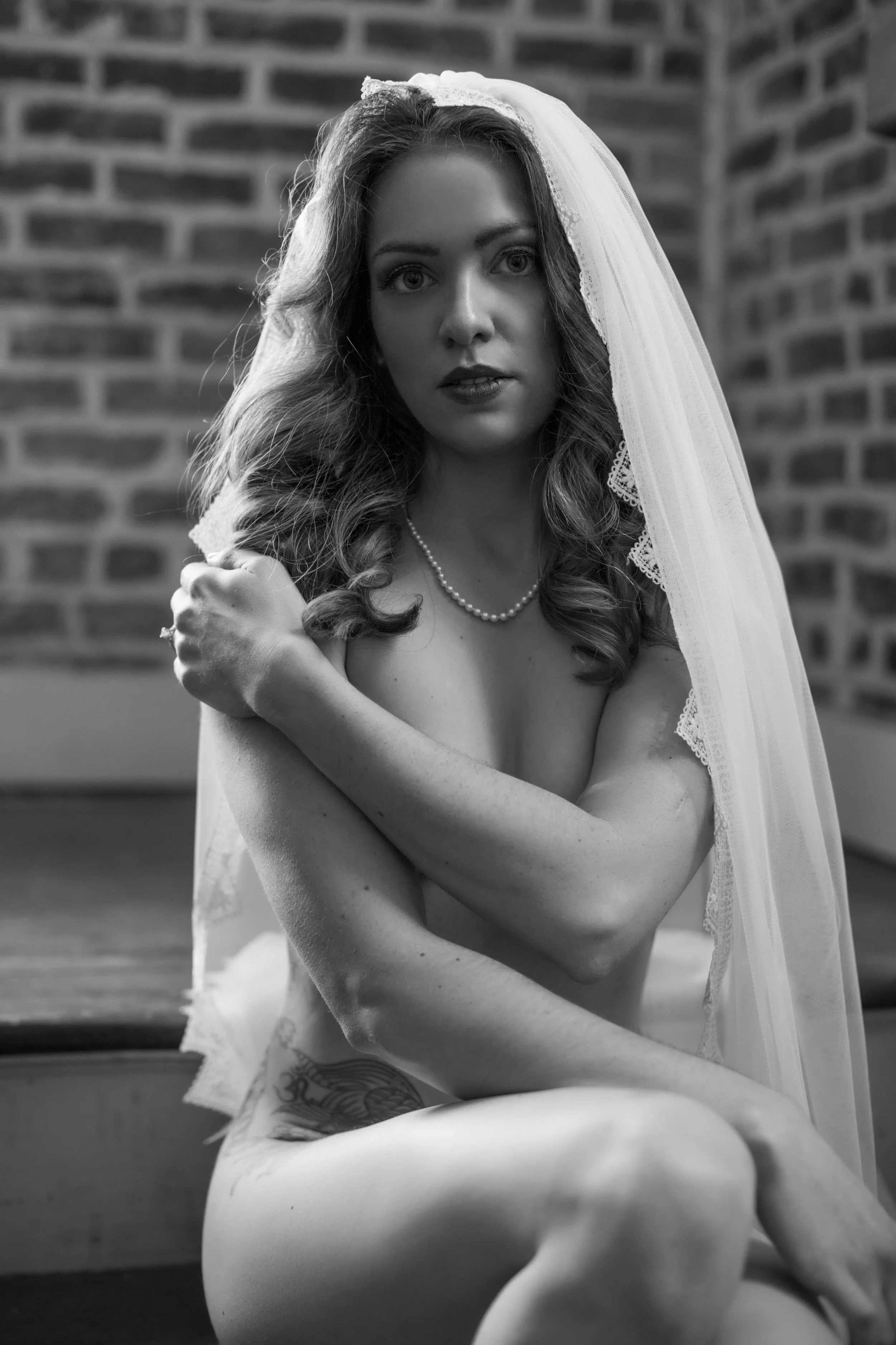 An intimate black and white bridal boudoir portrait of a bride with curly hair draped in a wedding veil, fine art photography by Emily Scott in Beaufort, South Carolina.