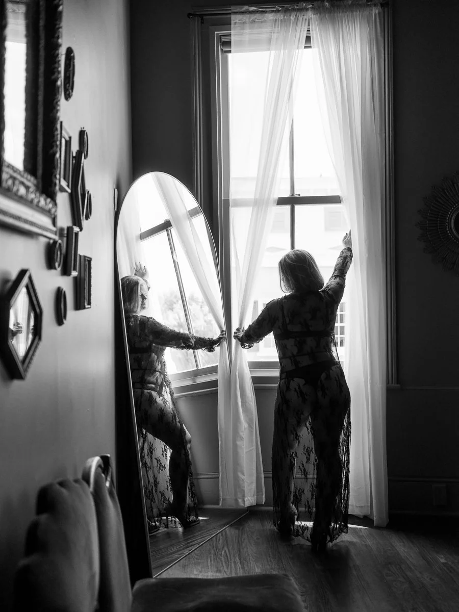 Woman in black lace lingerie looking out a window in natural light photographed by Emily Scott in Beaufort South Carolina
