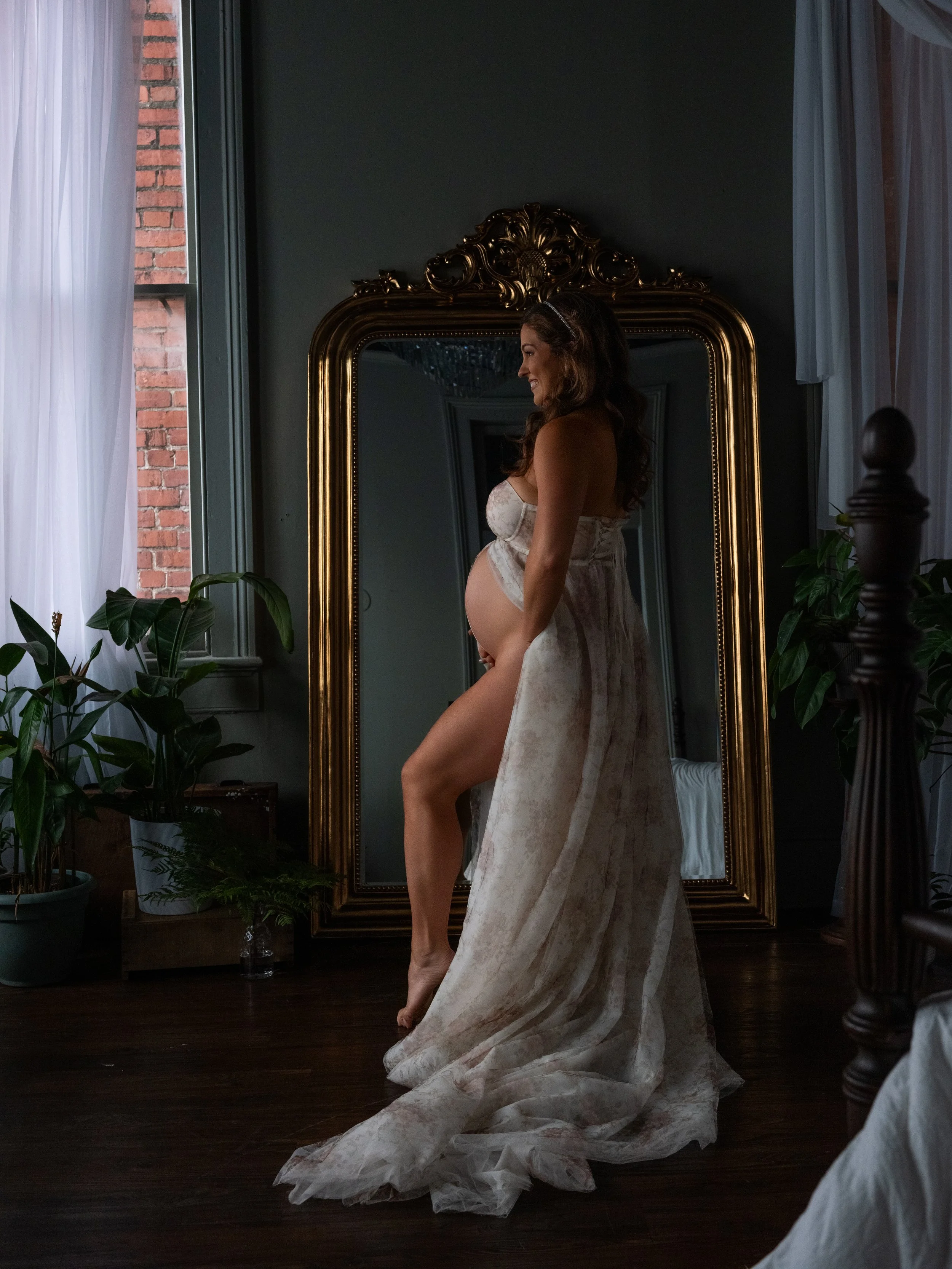 A romantic maternity boudoir portrait of a pregnant woman in floral draped fabric cradling her belly, photographed by Emily Scott in Beaufort, SC.