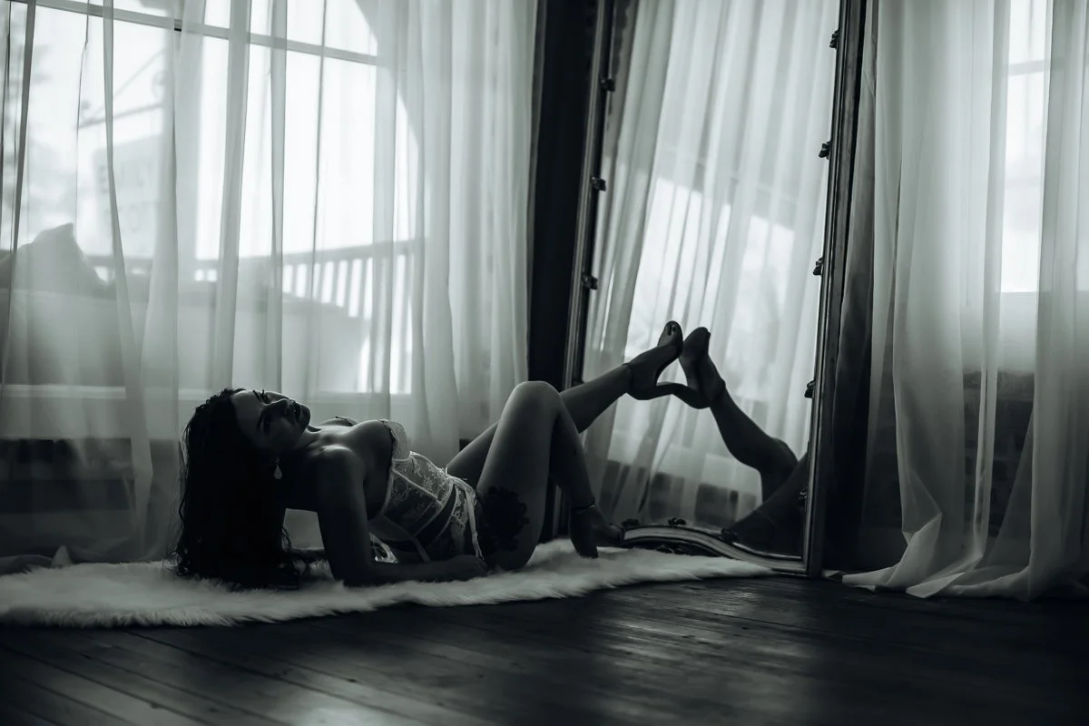 Black and white bridal boudoir portrait of a bride lying on a fur rug with legs raised near a mirror, Boudoir by Emily, Beaufort SC