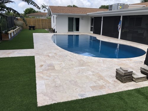 Travertine pool deck with artificial turf border in Jupiter, FL