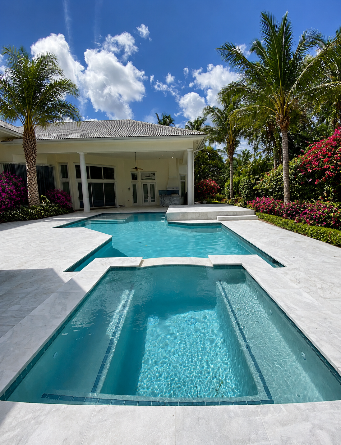 White marble pool deck framed by bougainvillea and palms, showcasing Big Cat Hardscapes craftsmanship.