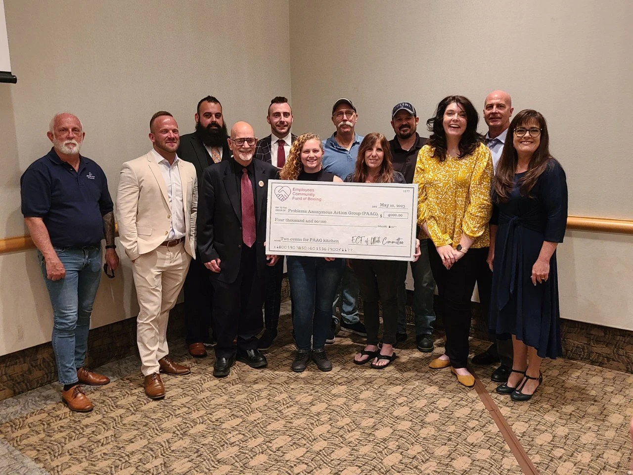 Group of people standing together indoors, holding a large check for $4,000 from Employees Community Fund of Boeing, celebrating a donation for PAAC kitchen project, smiling at the camera.