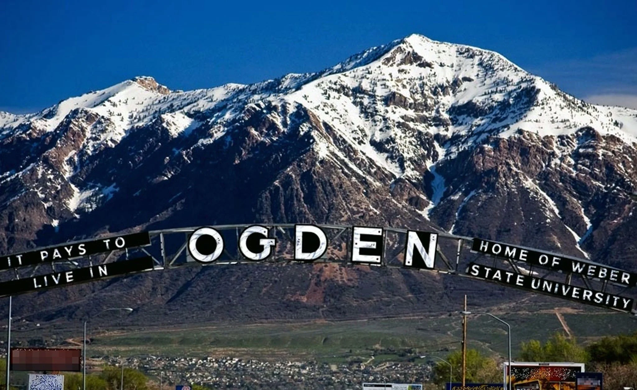 Sign in Ogden, Utah, with mountain landscape including snow-capped peaks and green fields below.