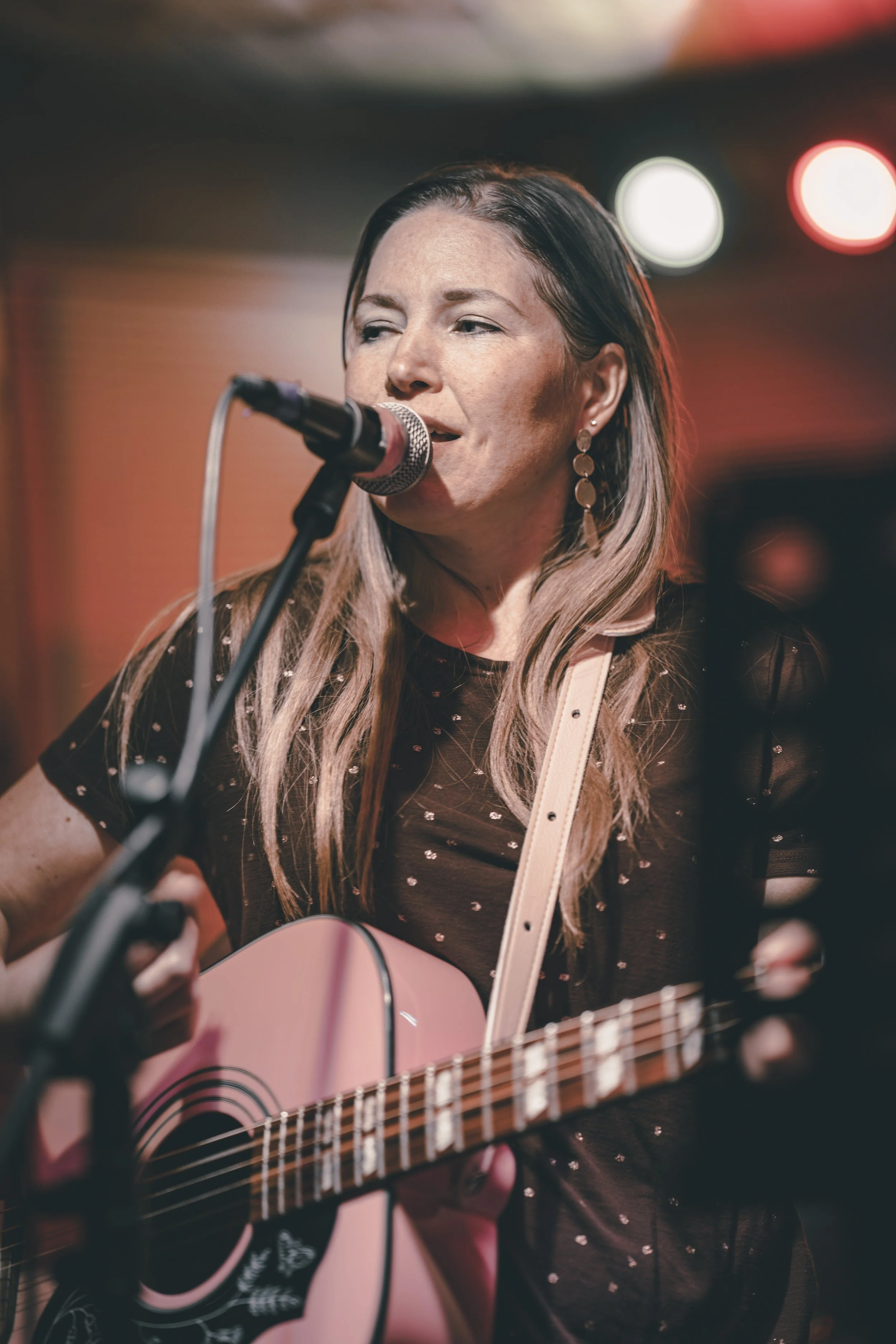 A woman singing into a microphone while playing an acoustic guitar on stage.