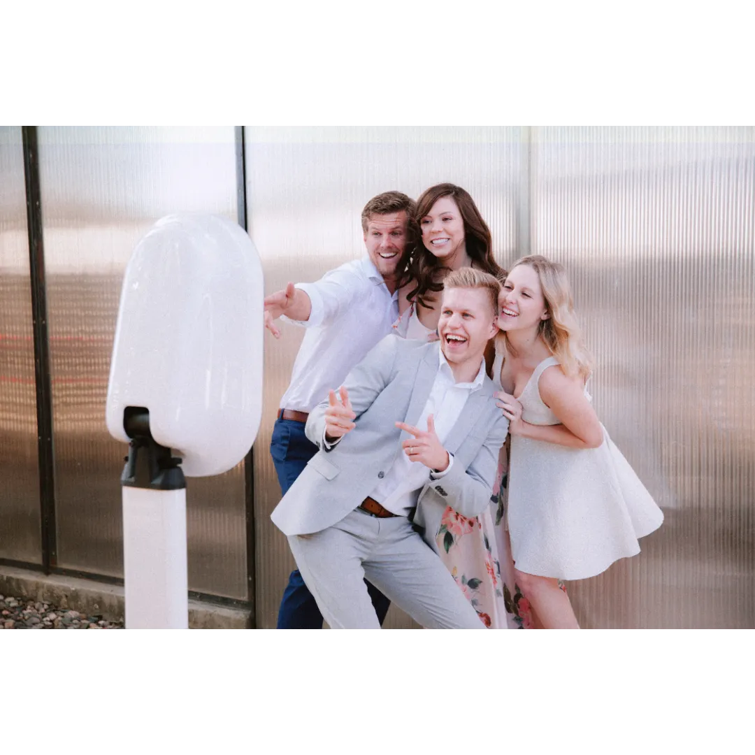 Four young adults, two men and two women, smiling and taking a selfie in front of a metallic wall.