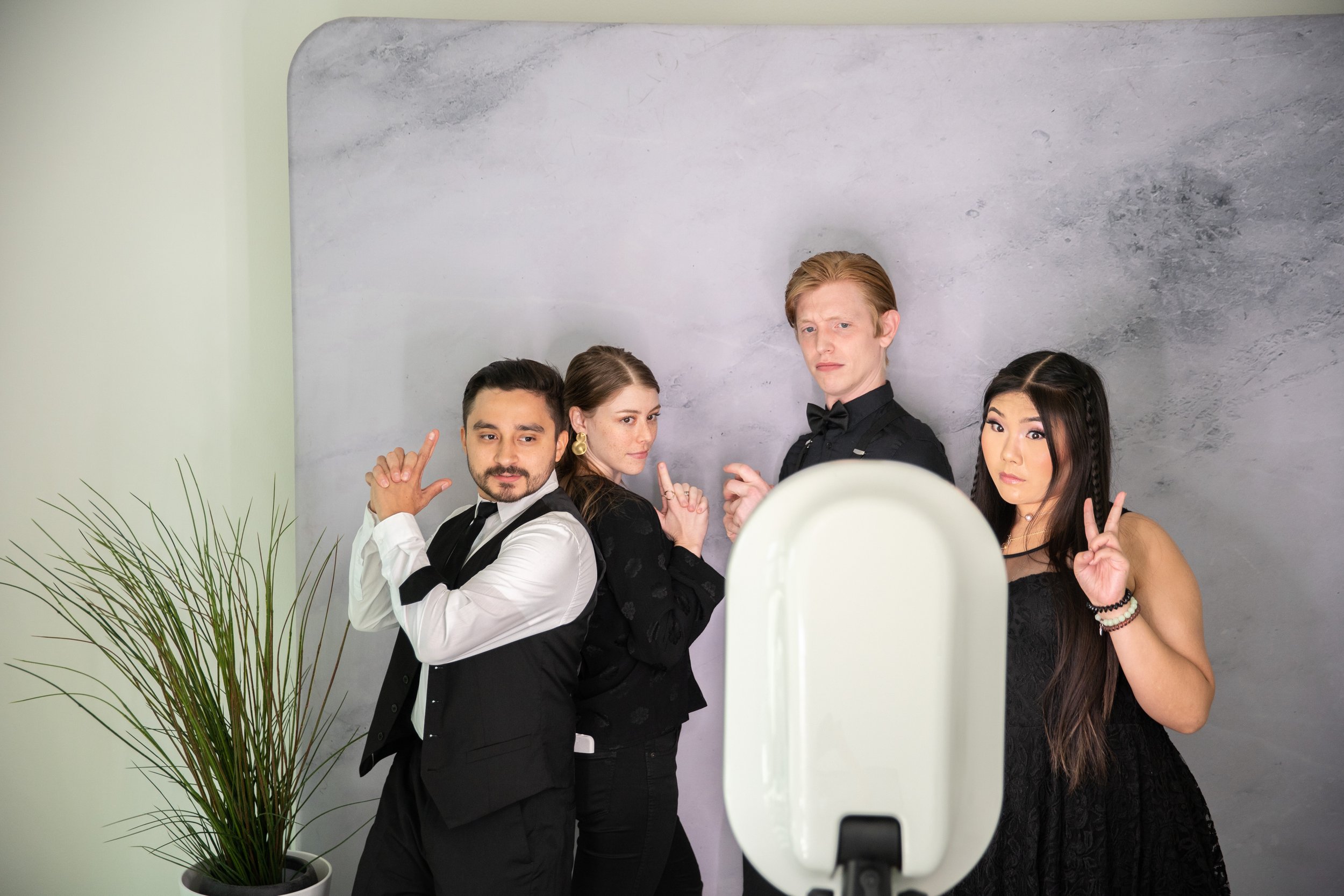 Four people posing for a photo in front of a gray background, making various hand gestures, with a white device in the foreground.