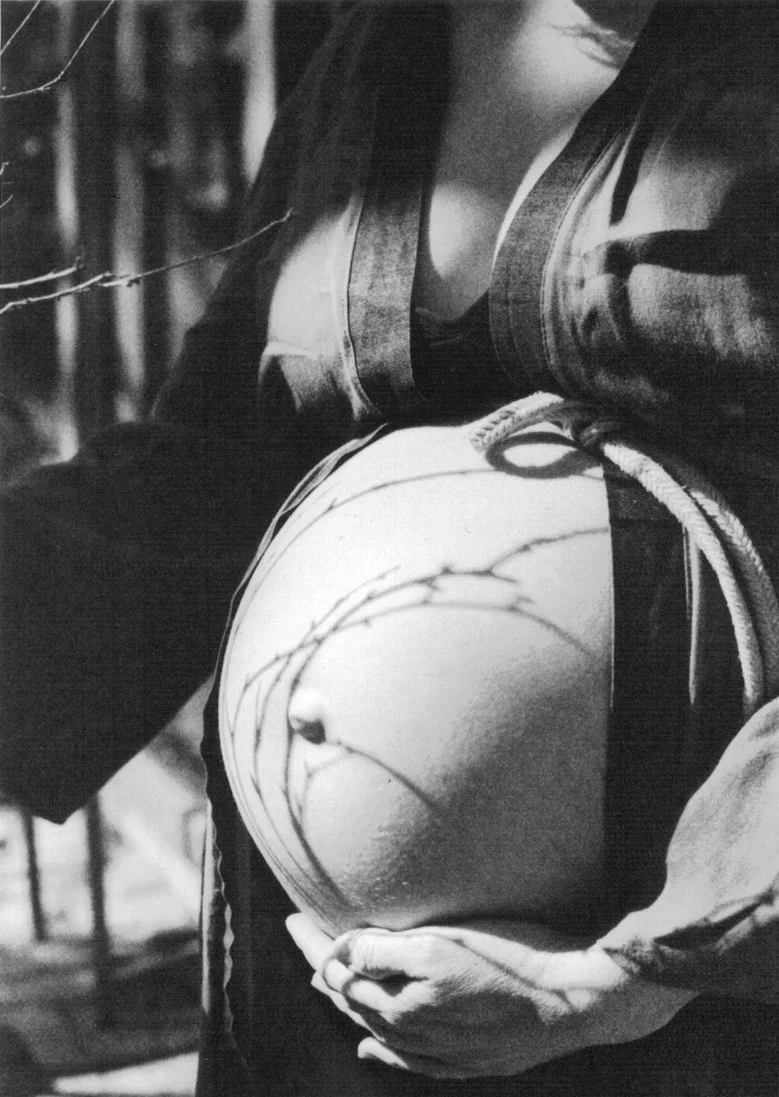 Close-up of a person holding a carved, rounded stone with barbed wire wrapped around it, dressed in a dark jacket and shirt.