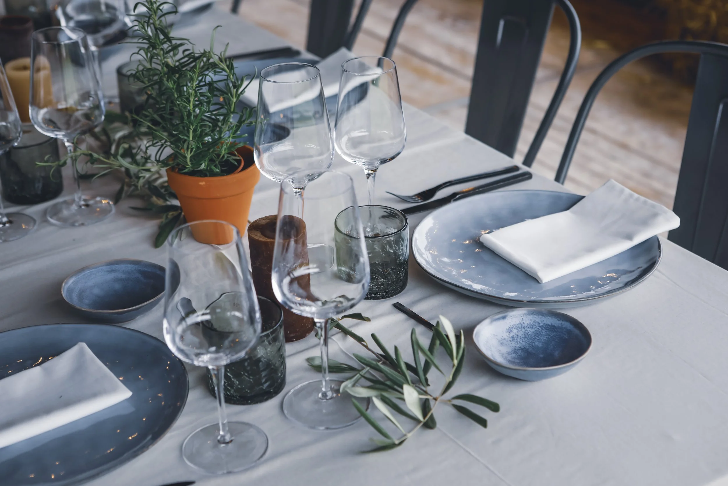A table setting with blue plates, white napkins, wine glasses, and decorative candles and greenery.