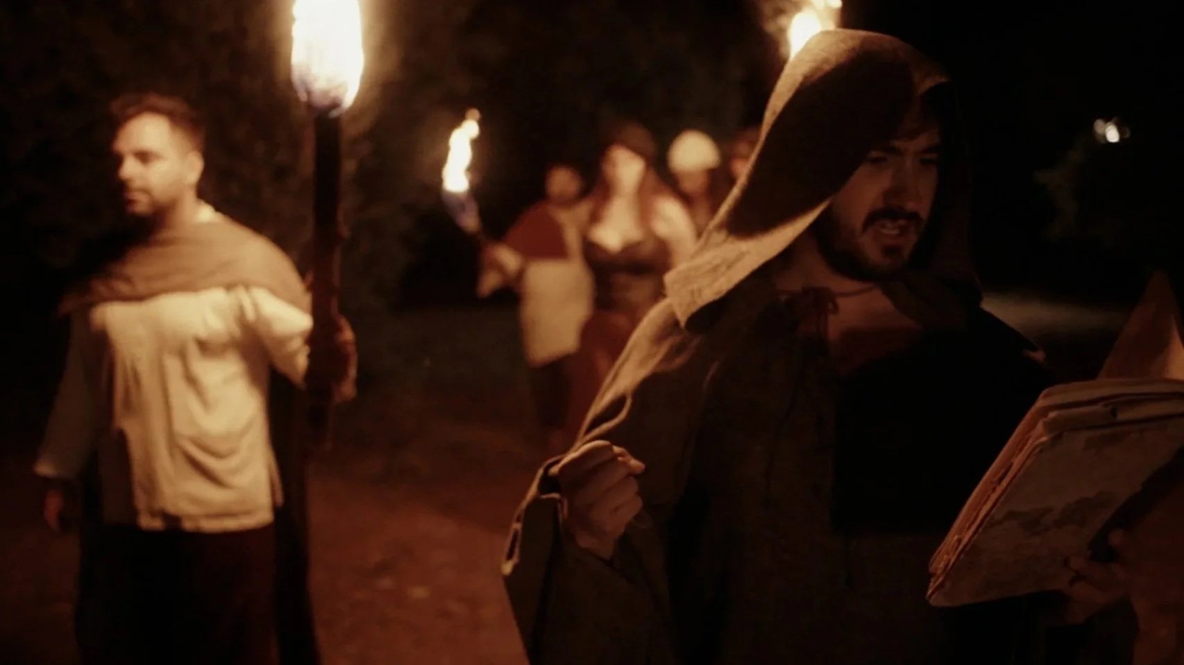 Personas con antorchas y un libro en una noche oscura, probablemente participando en una actividad o ritual al aire libre. Durante el rodaje de videoclip de la banda de Metal moderno, groove metal, metalcore y deathcore de madrid Rabia Perez.
