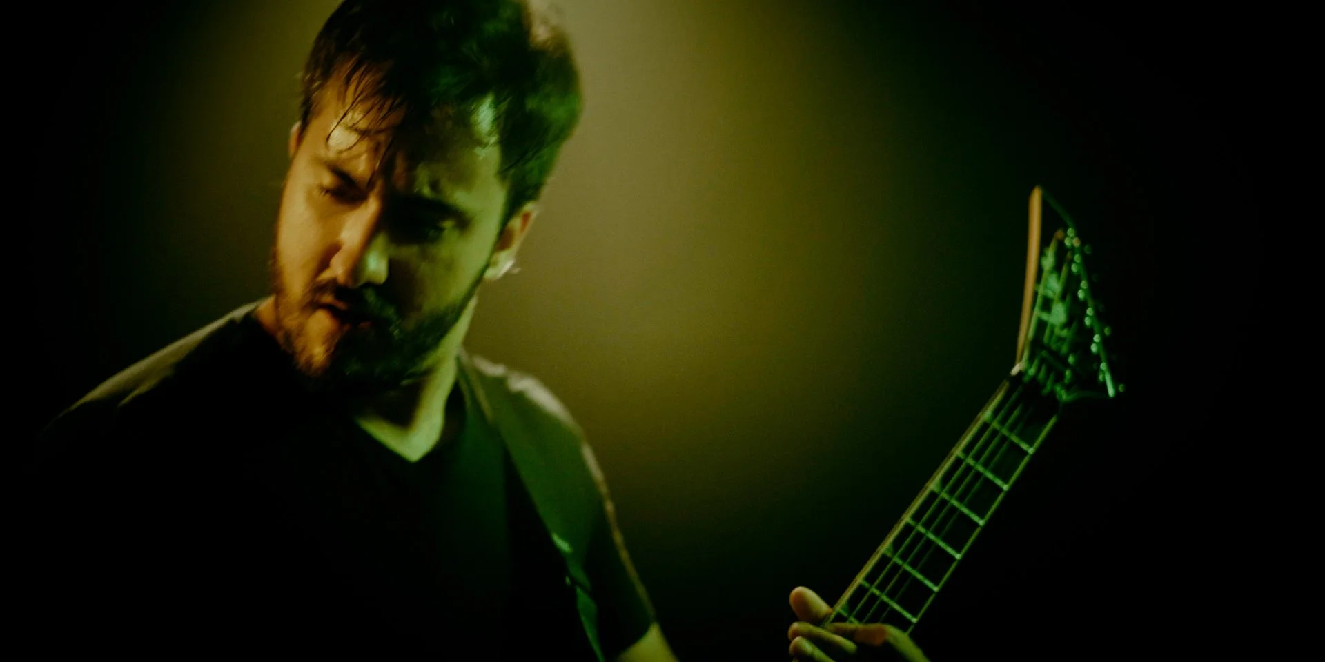Hombre tocando Metal moderno, groove metal, metalcore y deathcore en guitarra eléctrica Jackson con luces verdes y ambiente oscuro en el rodaje del videoclip de la banda de madrid Rabia Perez.