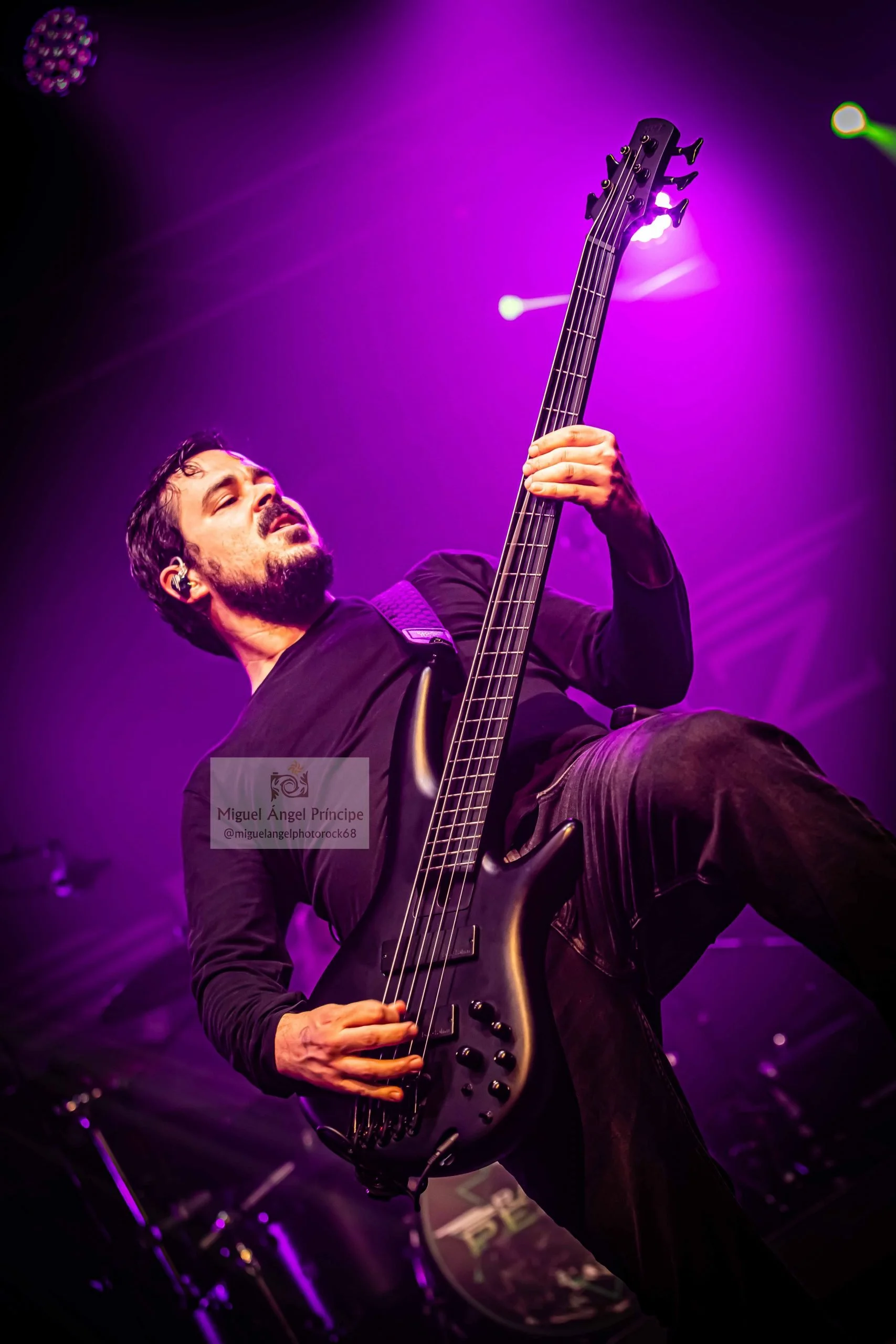 Un hombre tocando Metal moderno, groove metal, metalcore y deathcore en un bajo eléctrico en un escenario con iluminación púrpura en Madrid.