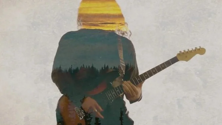 Una persona tocando una guitarra eléctrica, con un efecto de doble exposición que muestra un paisaje de árboles y un atardecer. Madrid. Metalcore, metal moderno, groove metal y deathcore.