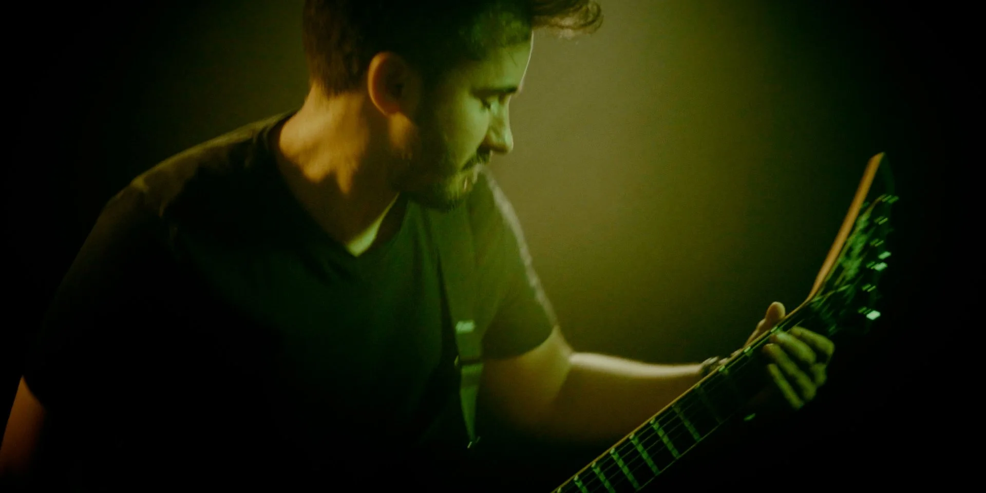 Joven tocando Metal moderno, groove metal, metalcore y deathcore en la guitarra electrica Jackson en un ambiente oscuro con luz verde en el rodaje del videoclip de la banda Rabia Perez en Madrid.